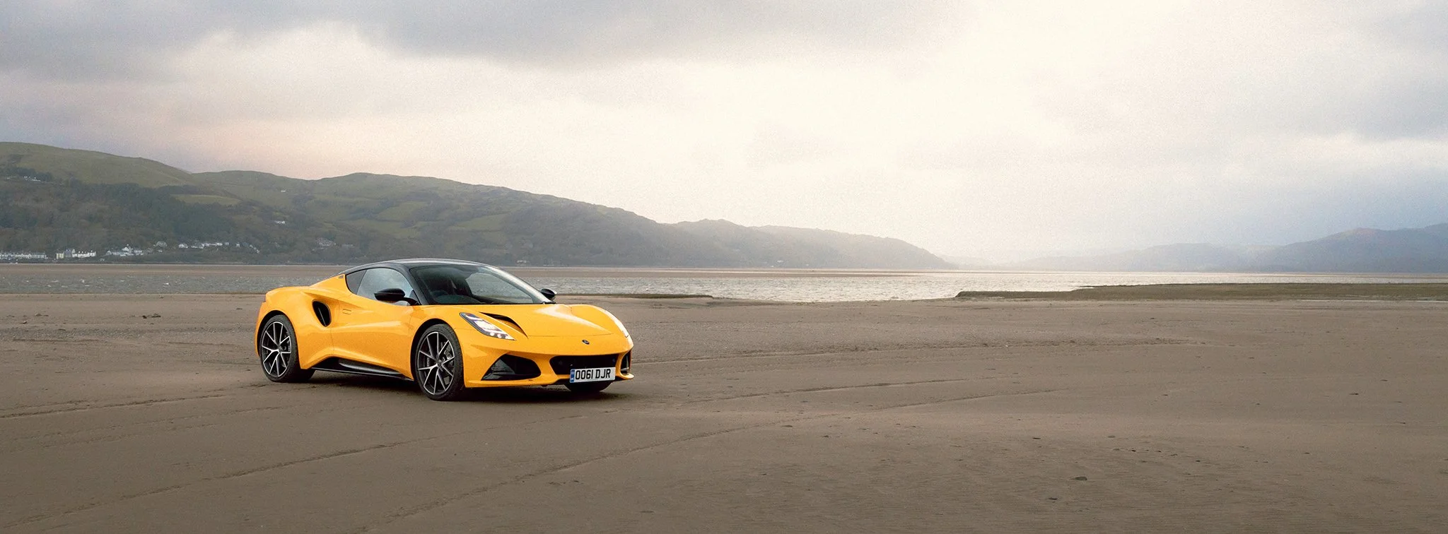 A yellow Lotus Emira on a beach in a Welsh valley
