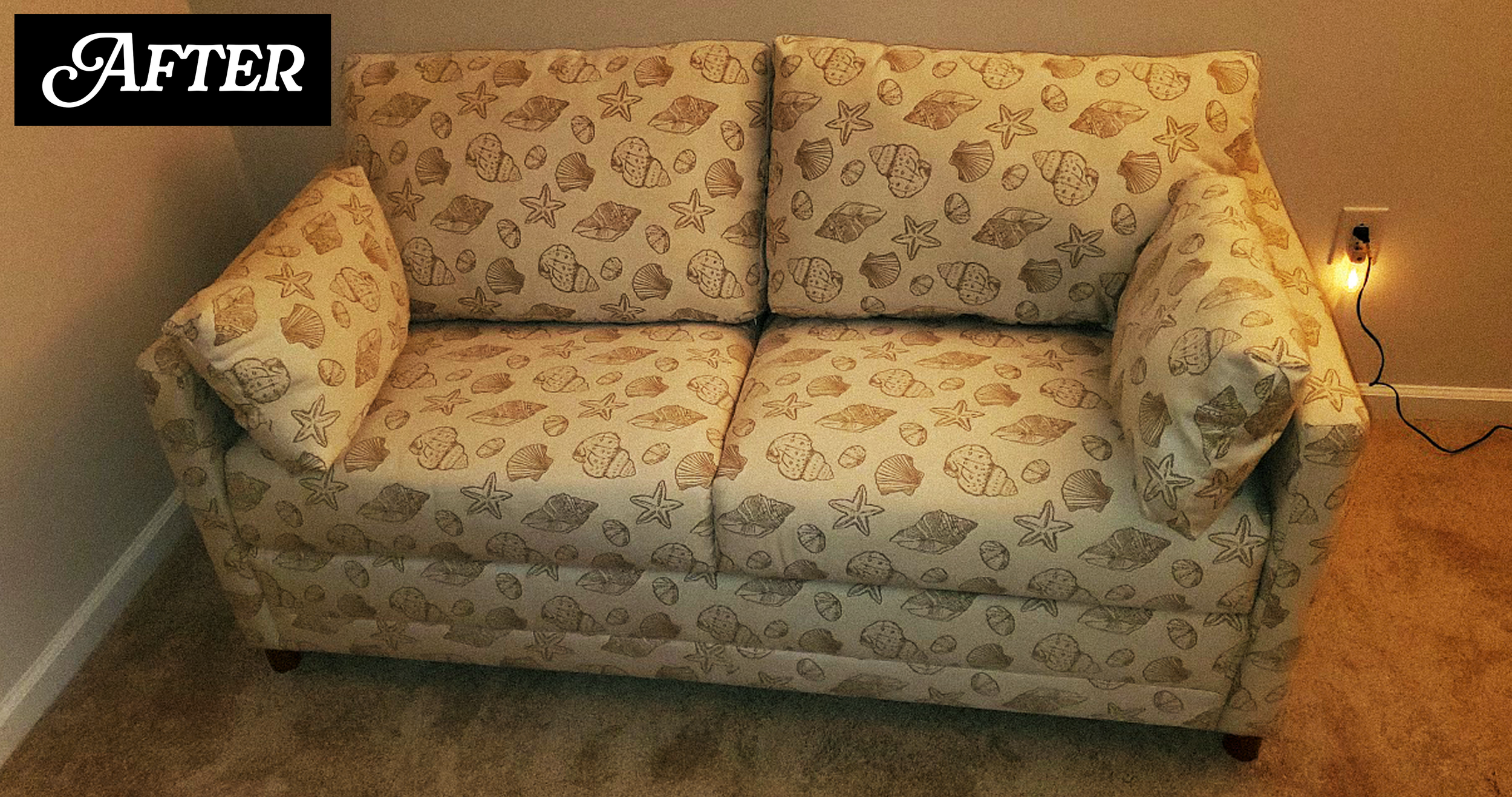 A beige sofa with seashell and starfish patterns, placed against a plain wall in a room. To the right, a floor lamp with a yellow glow is plugged into an outlet.