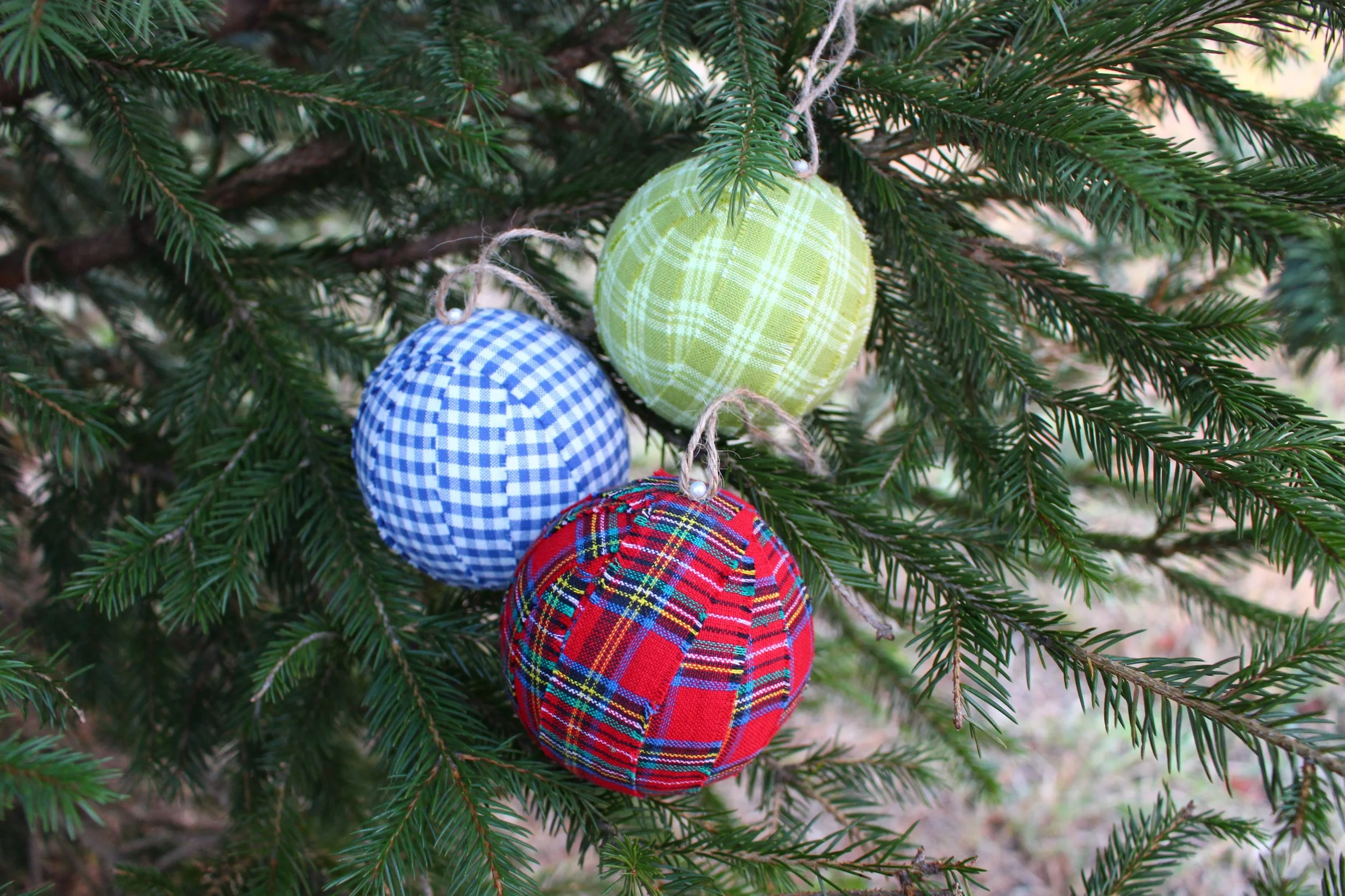 Red, green, and blue plaid Christmas ball ornaments hanging on tree branch