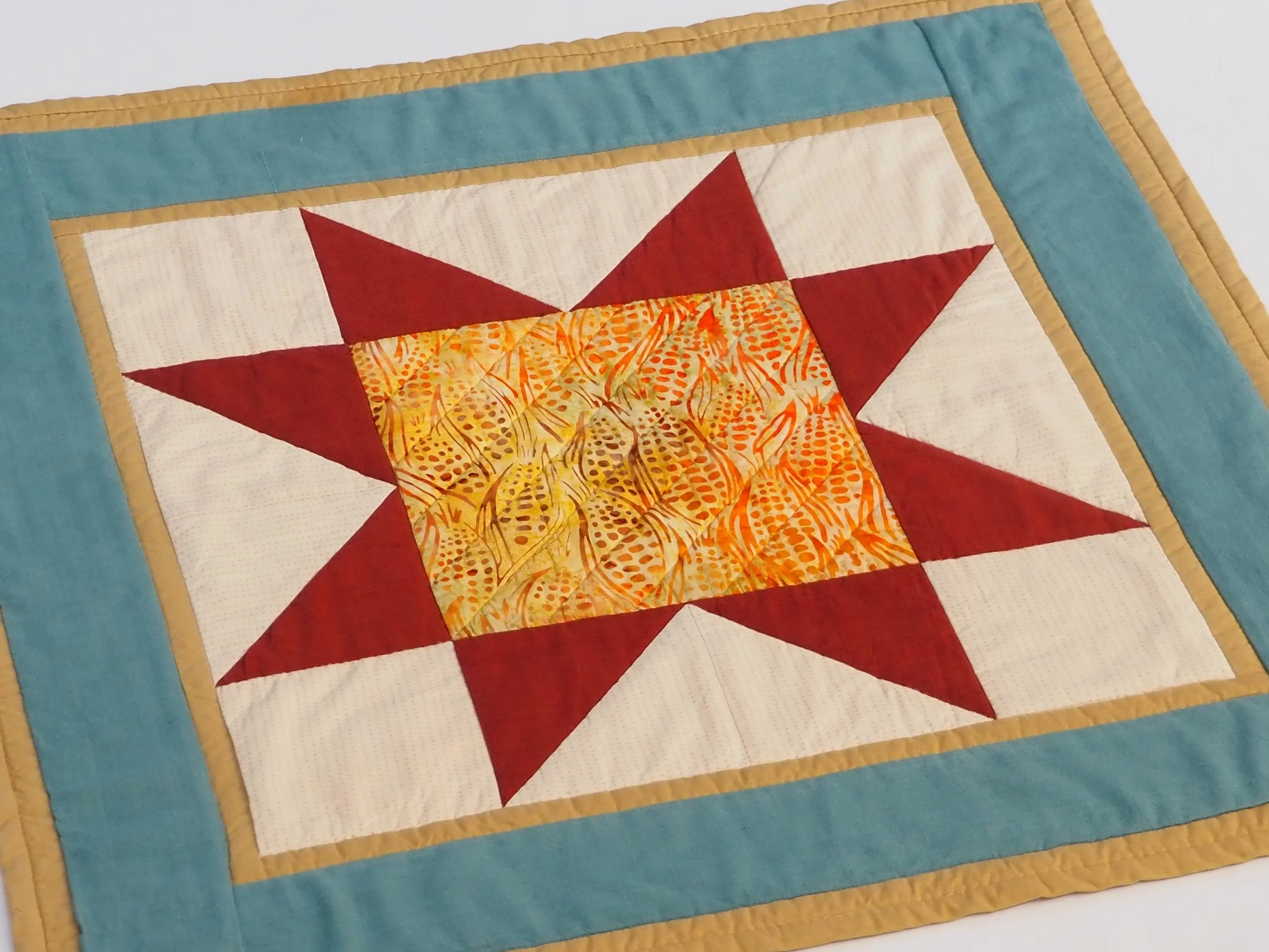 Square quilted table topper with batik indian corn center, red star points, and teal gold borders