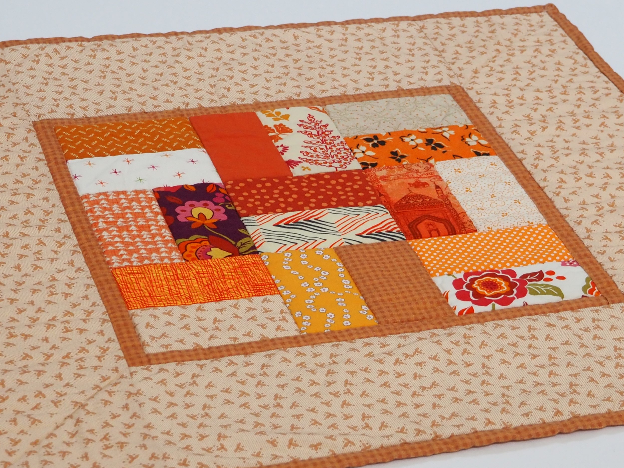 Orange patchwork quilted table topper measuring 22 by 22 inches on a dining table