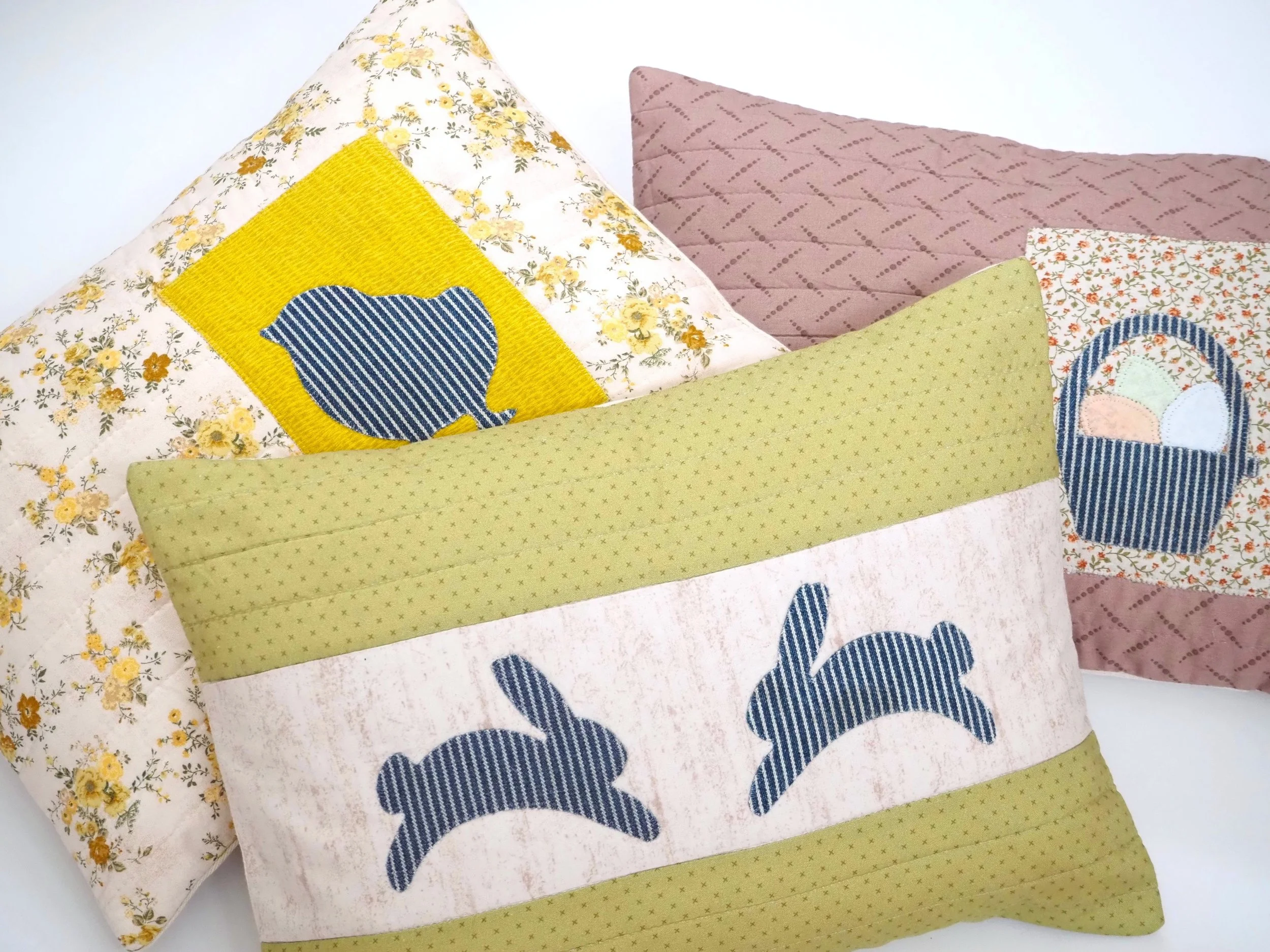 Four decorative pillows with Easter and springtime designs, including bunnies and Easter baskets, positioned on a white surface.