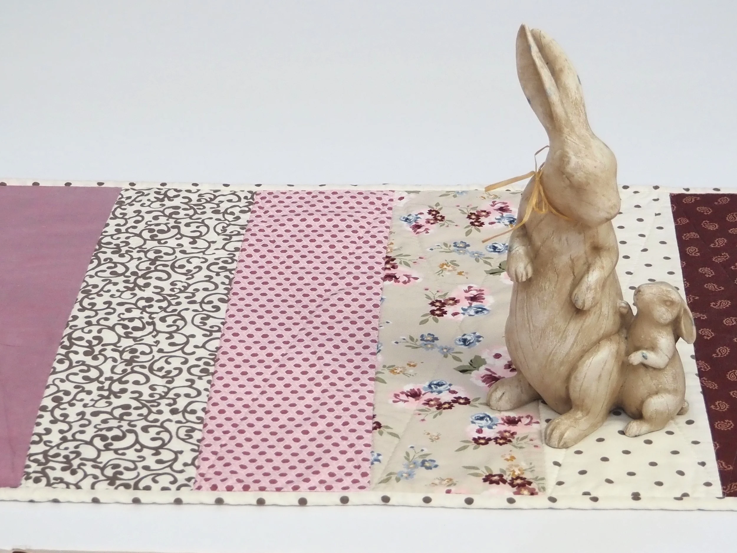 Handmade burgundy and pink striped quilted table runner on a wooden dining table.