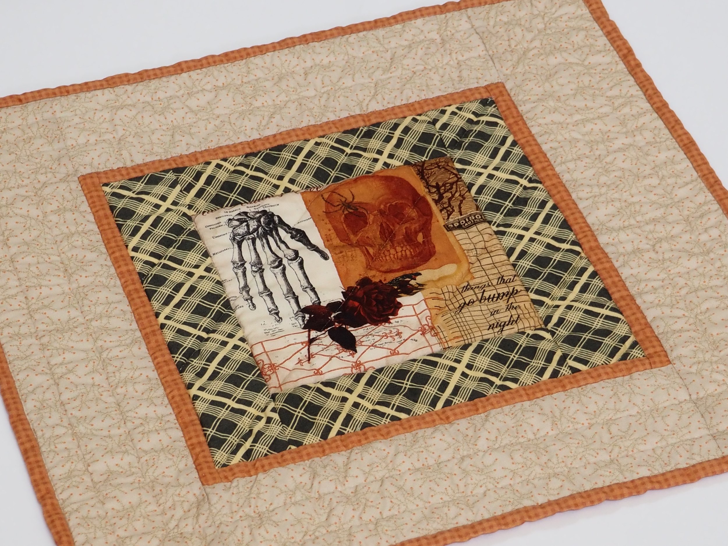 Handcrafted 19.5 inch square Halloween quilted table topper featuring a black plaid and orange fabric border.