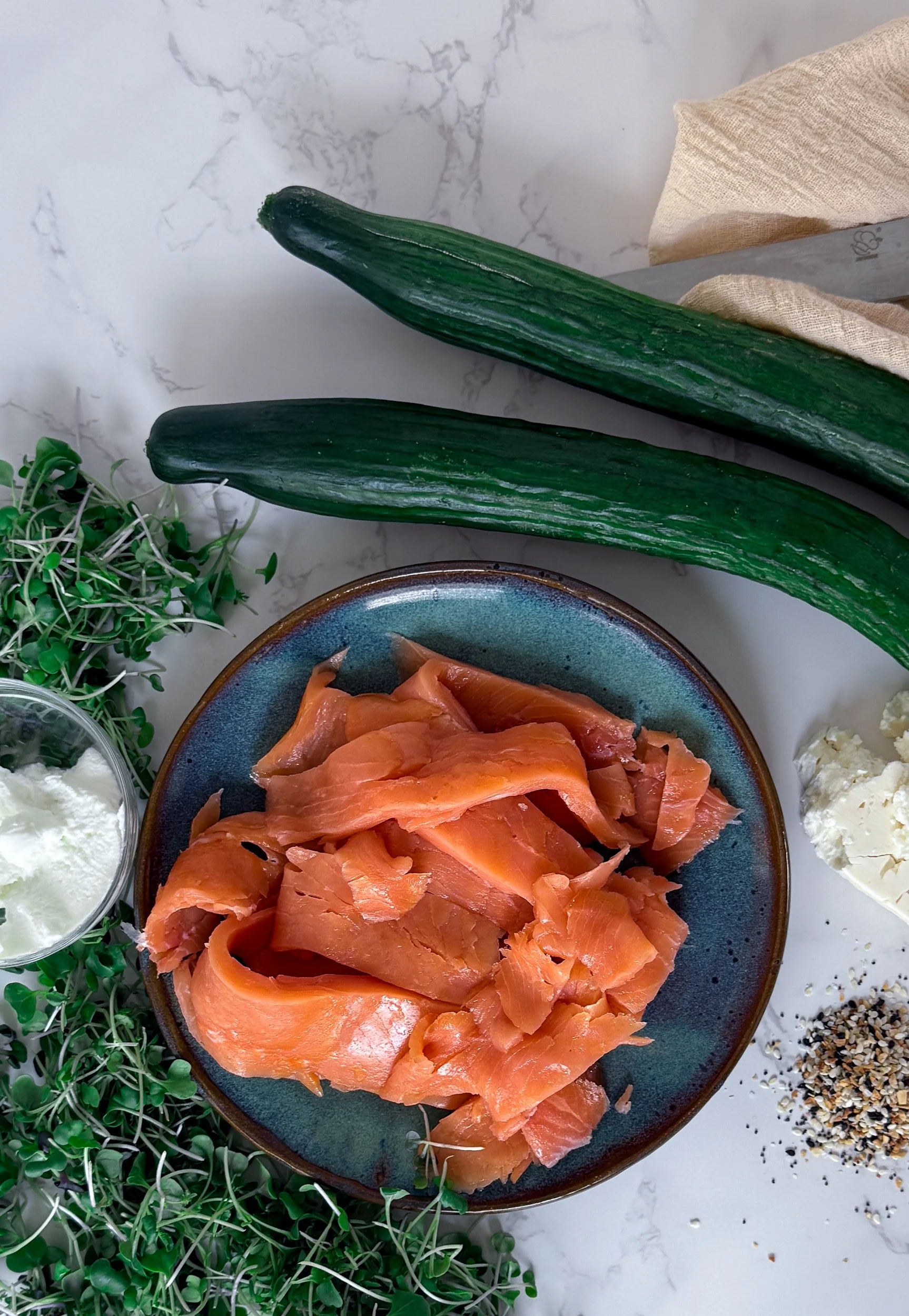 Fresh ingredients for Mediterranean cucumber boats including whole English cucumbers, smoked salmon ribbons, feta cheese, Greek yogurt, a lemon, and everything bagel seasoning.