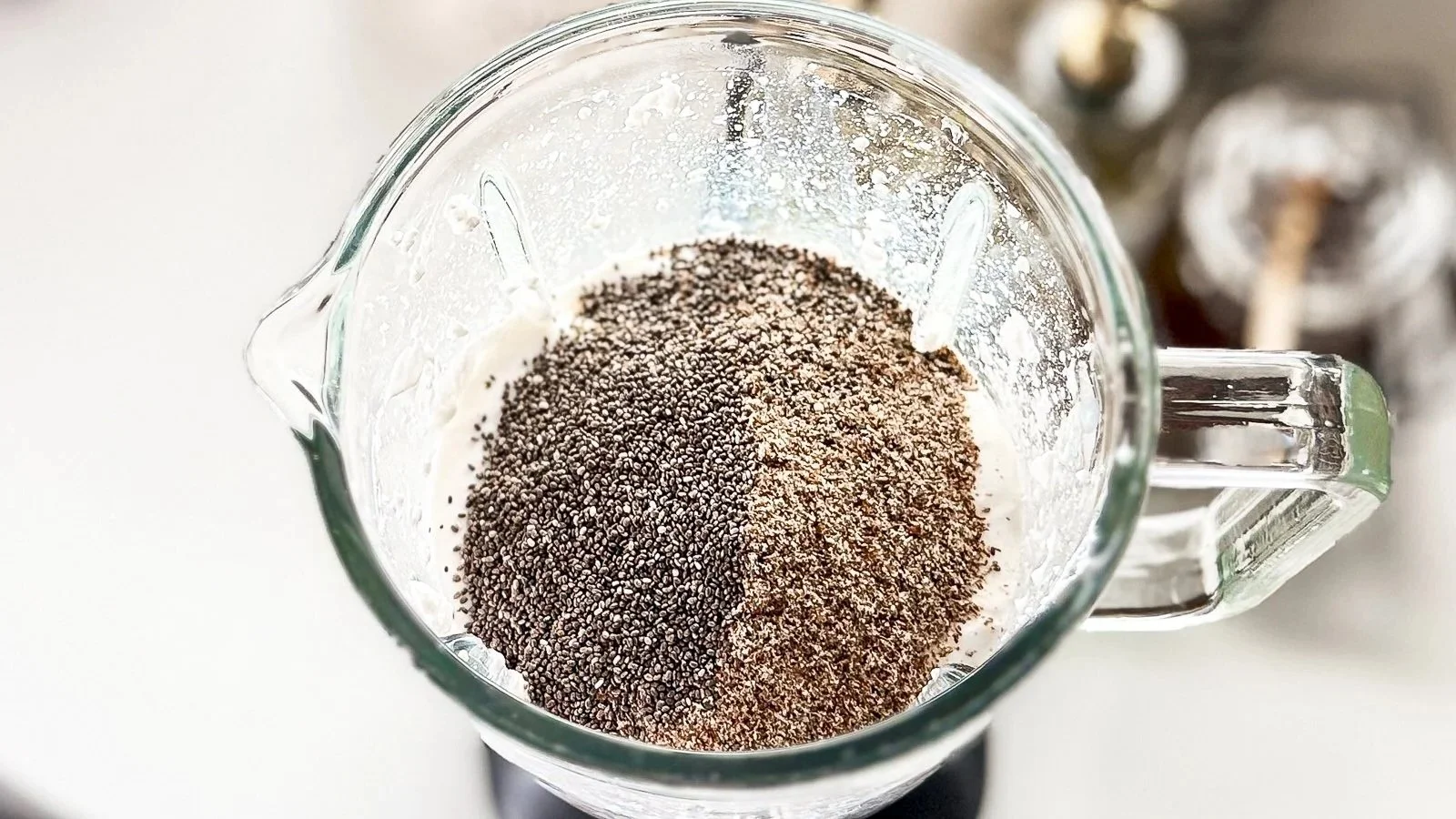 A top‑down view of a blender filled with yogurt, chia seeds, and flaxseed before blending.