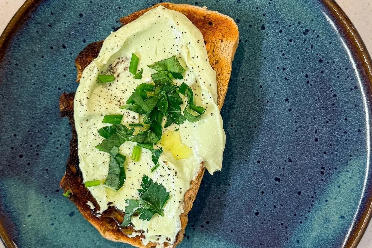 whipped avocado and cottage cheese on sourdough toast with olive oil, fresh herbs, and black pepper
