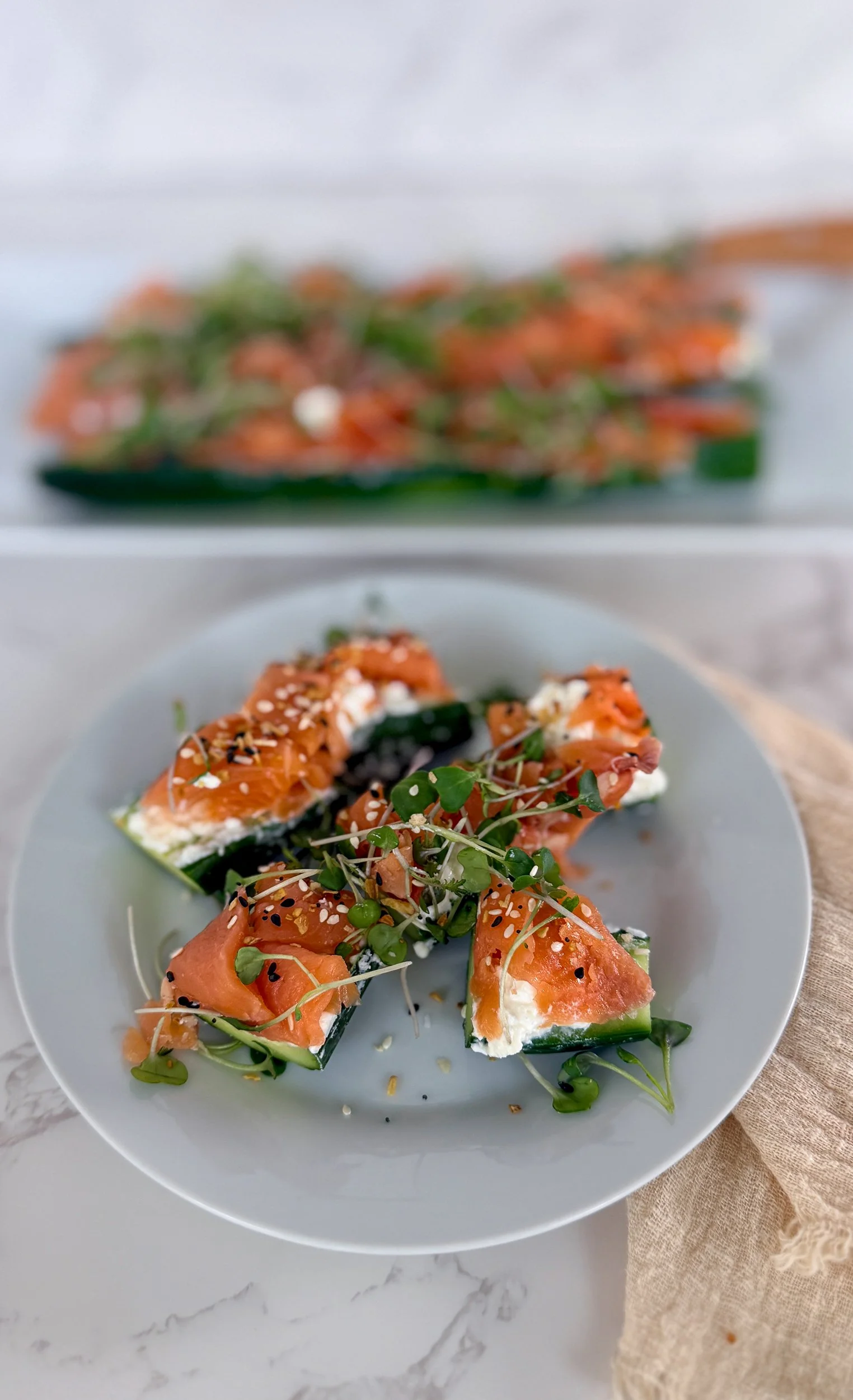 A close-up, macro shot of sliced cucumber rounds showing the texture of lemon-zested whipped feta mousse, silky smoked salmon, and a sprinkle of everything bagel seasoning.