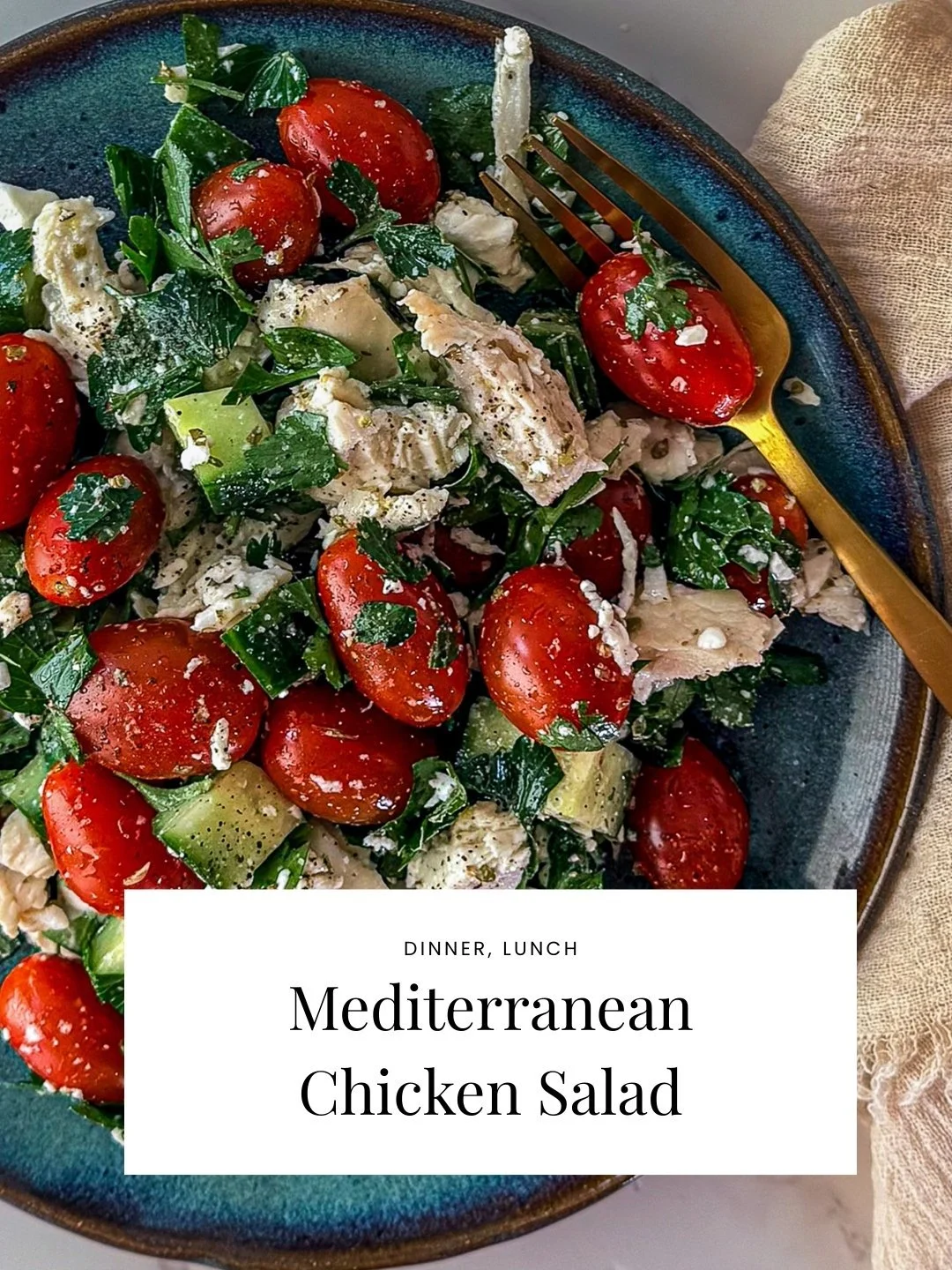 Close-up of a Mediterranean chicken salad with cherry tomatoes, chopped lettuce, cucumbers, pieces of chicken, and crumbled cheese on a dark blue plate.