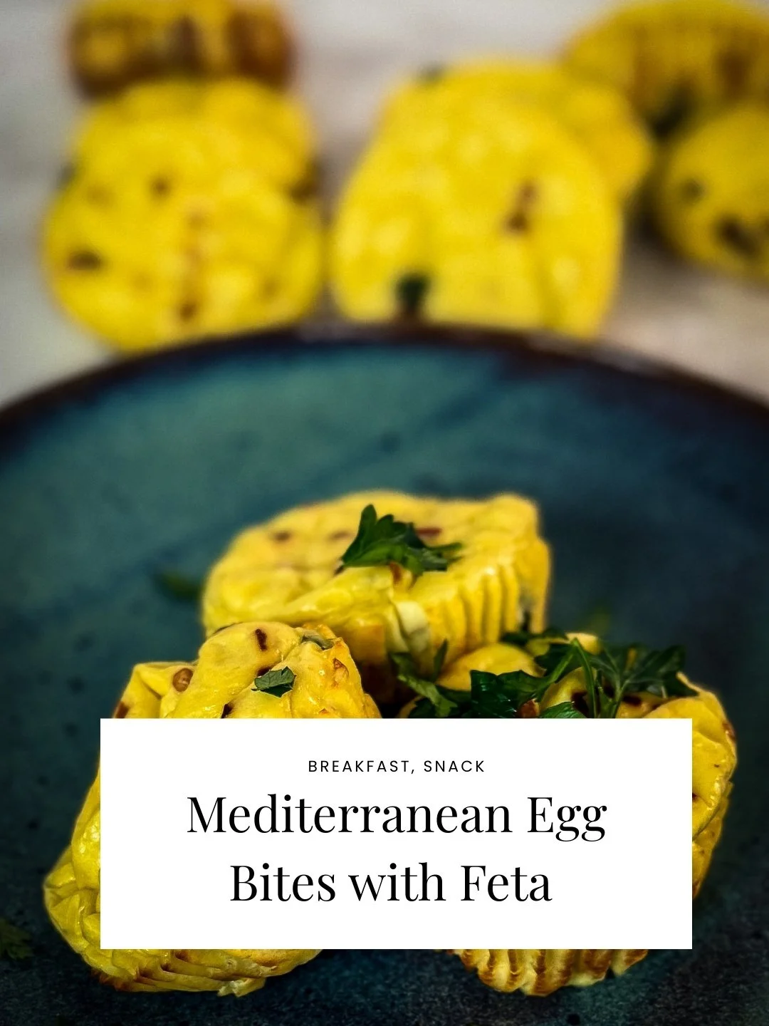 Close-up of Mediterranean egg bites with feta cheese garnished with parsley, on a dark plate, with more eggs in the background.