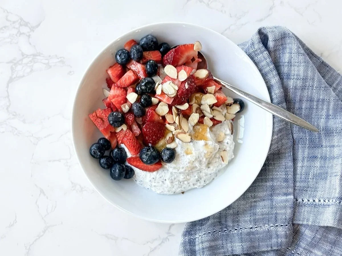 Bowl of chia pudding topped with strawberries, blueberries, sliced almonds, and a light honey drizzle on a marble surface.