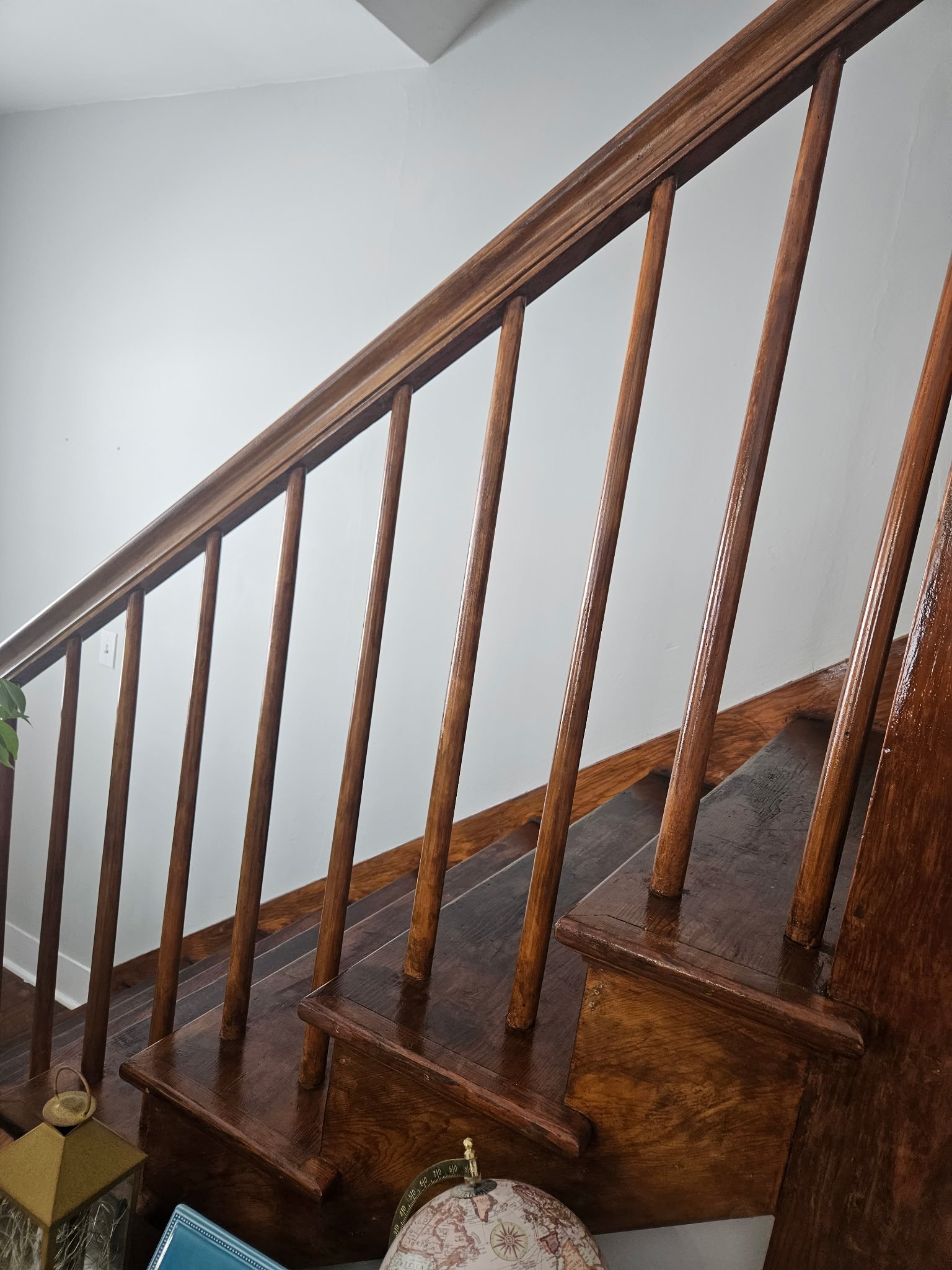 Wooden staircase with vertical balusters and a handrail, leading upward inside a home with white walls.