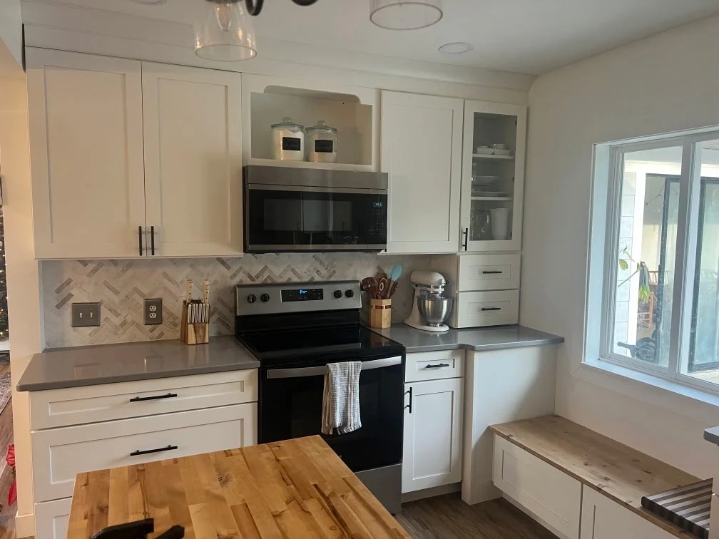 Modern kitchen with white cabinets, gray countertops, stainless steel appliances, and a window seat.