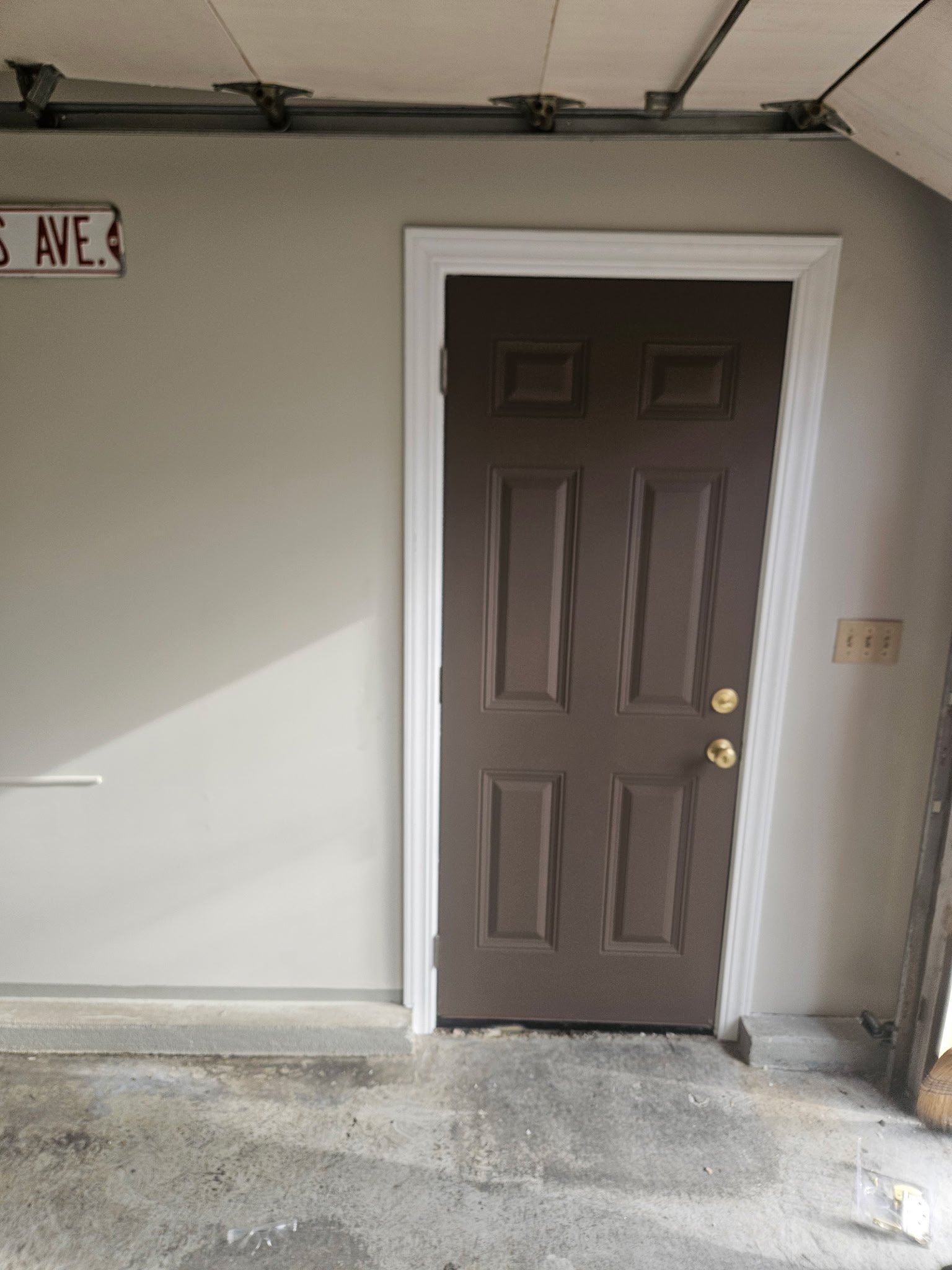 A brown door with six rectangular panels, white trim, in a garage or utility room with unfinished concrete floor.