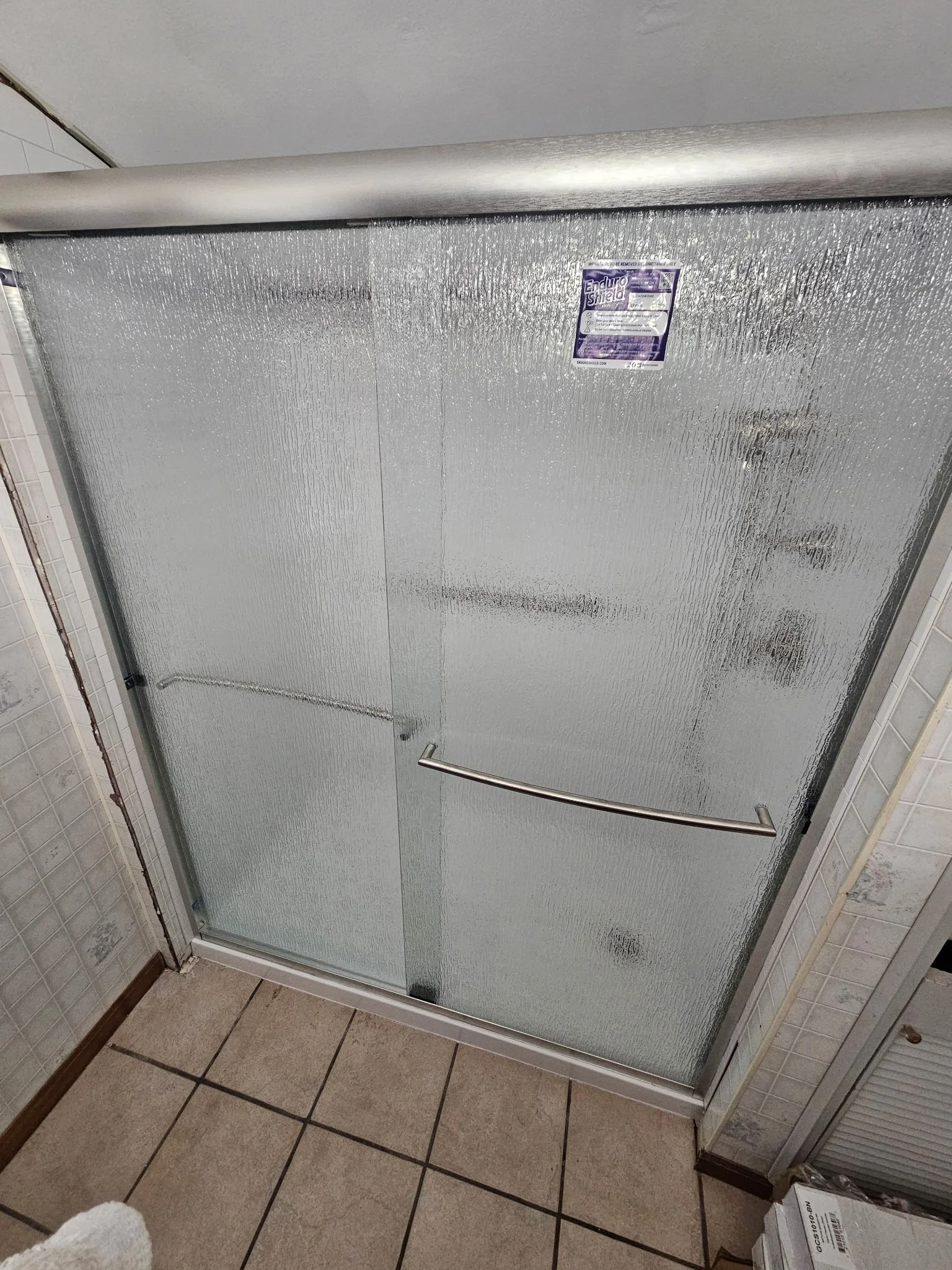 Shower door with textured glass and a metal handle in a tiled bathroom.