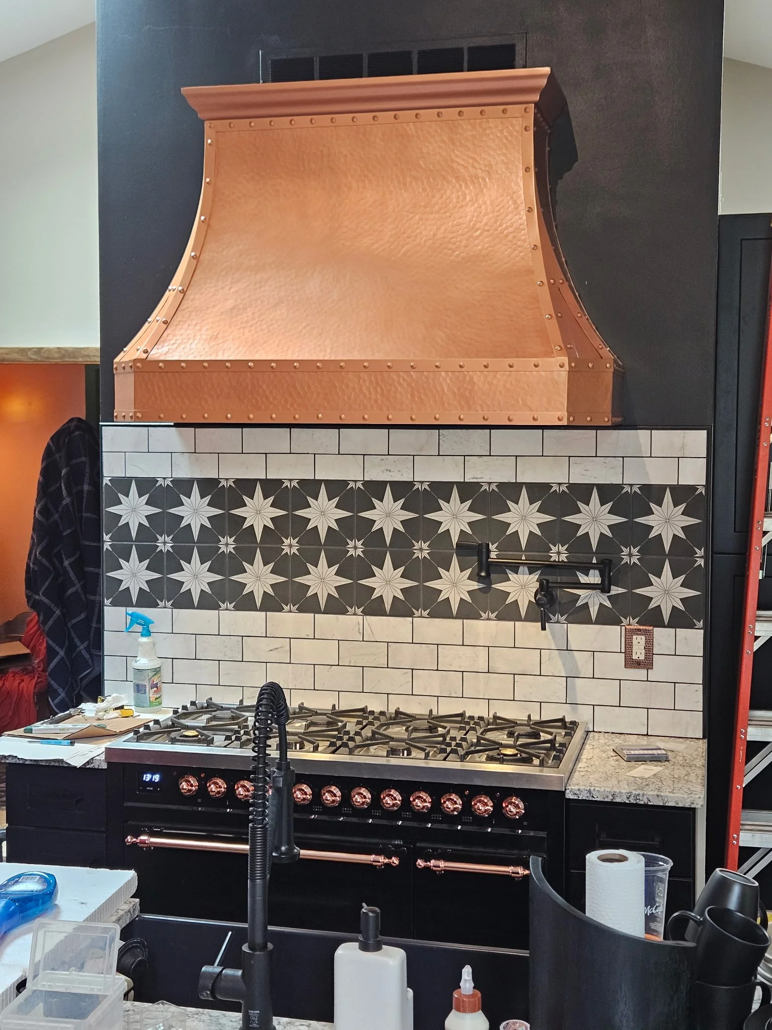Kitchen stove with a copper range hood and decorative tile backsplash.