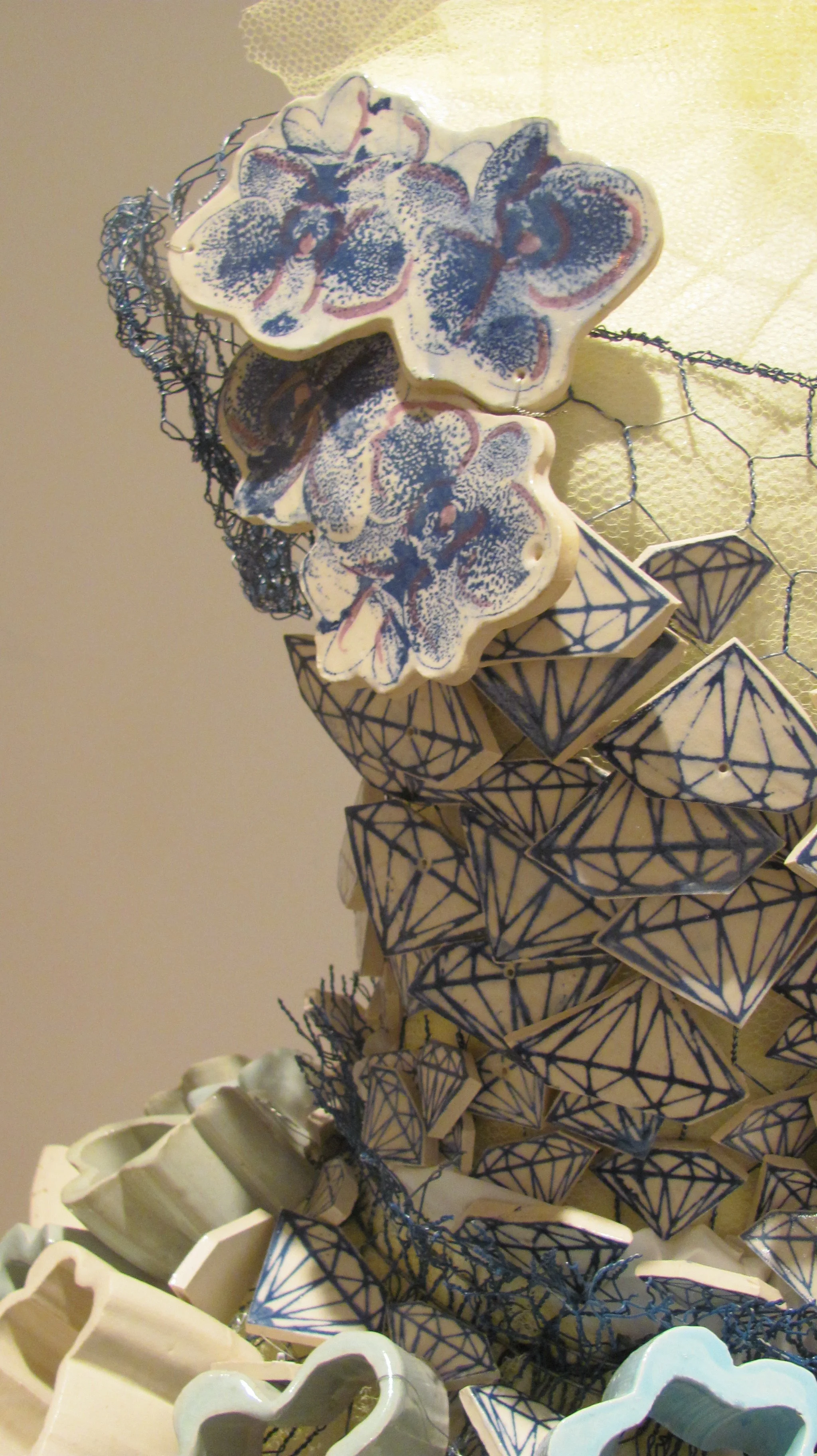 Decorative ceramic objects with floral and diamond patterns, arranged on a wire mesh surface.