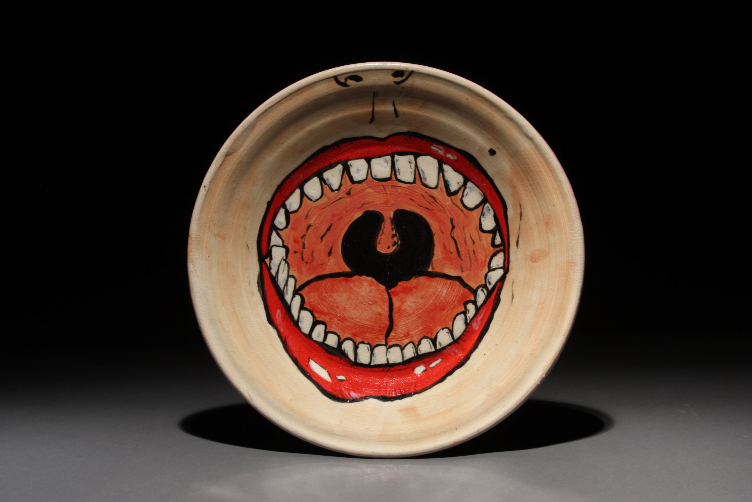 Ceramic plate with a colorful, cartoonish depiction of an open mouth with teeth, tongue, and red lips, set against a black background.