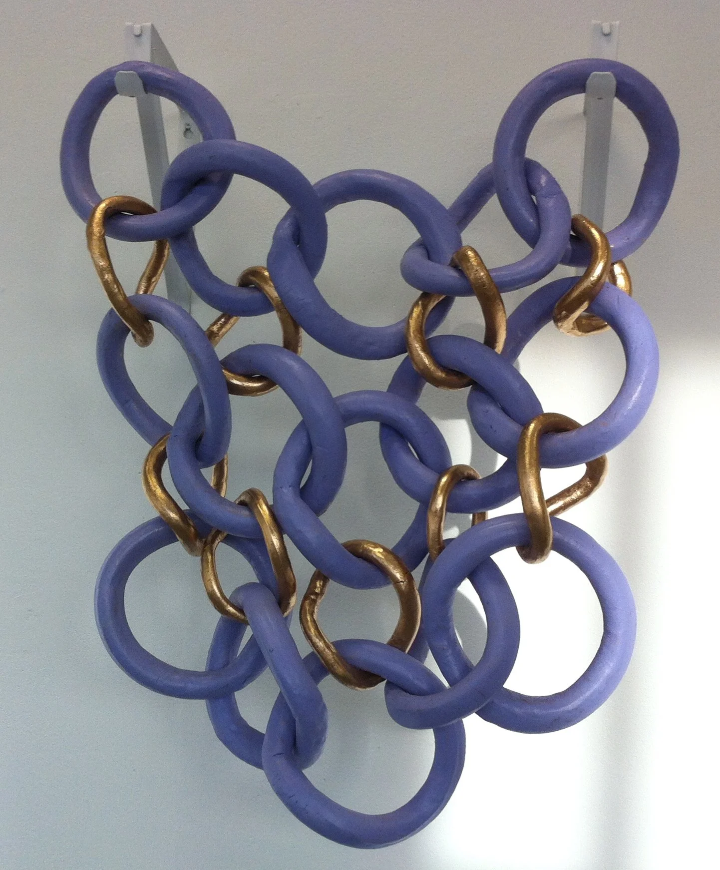 An abstract sculpture made of large purple and gold interconnected rings hanging on a wall.
