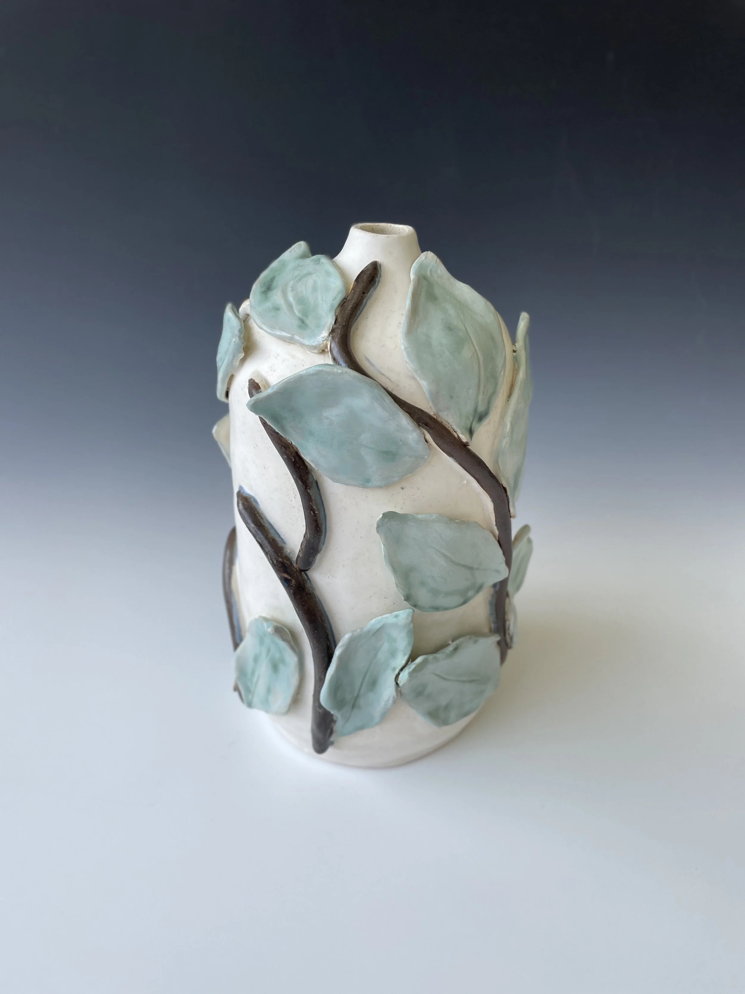 Ceramic vase with sculpted green leaves and dark brown vines.