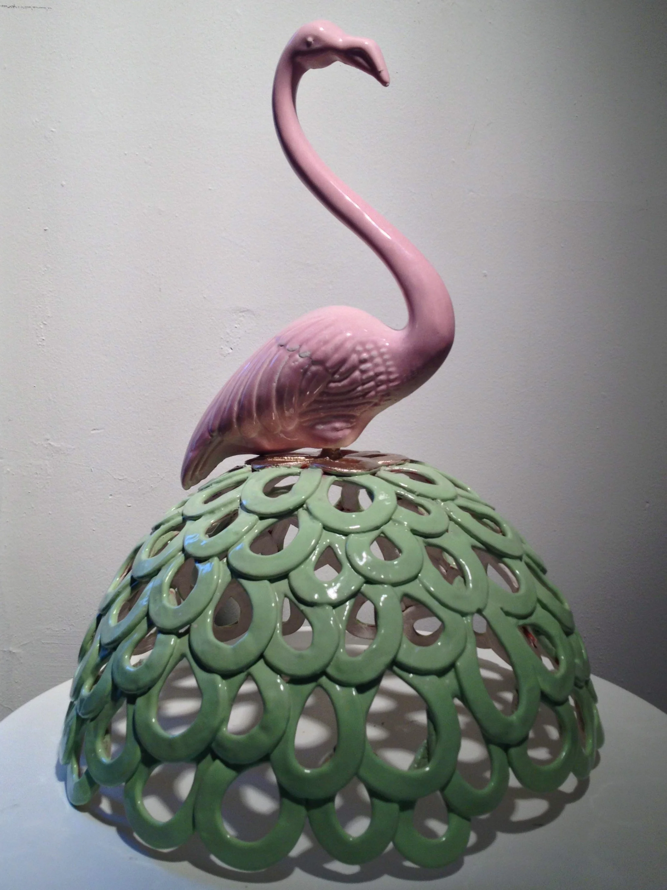 Ceramic sculpture of a pink flamingo standing on a green, openwork base.