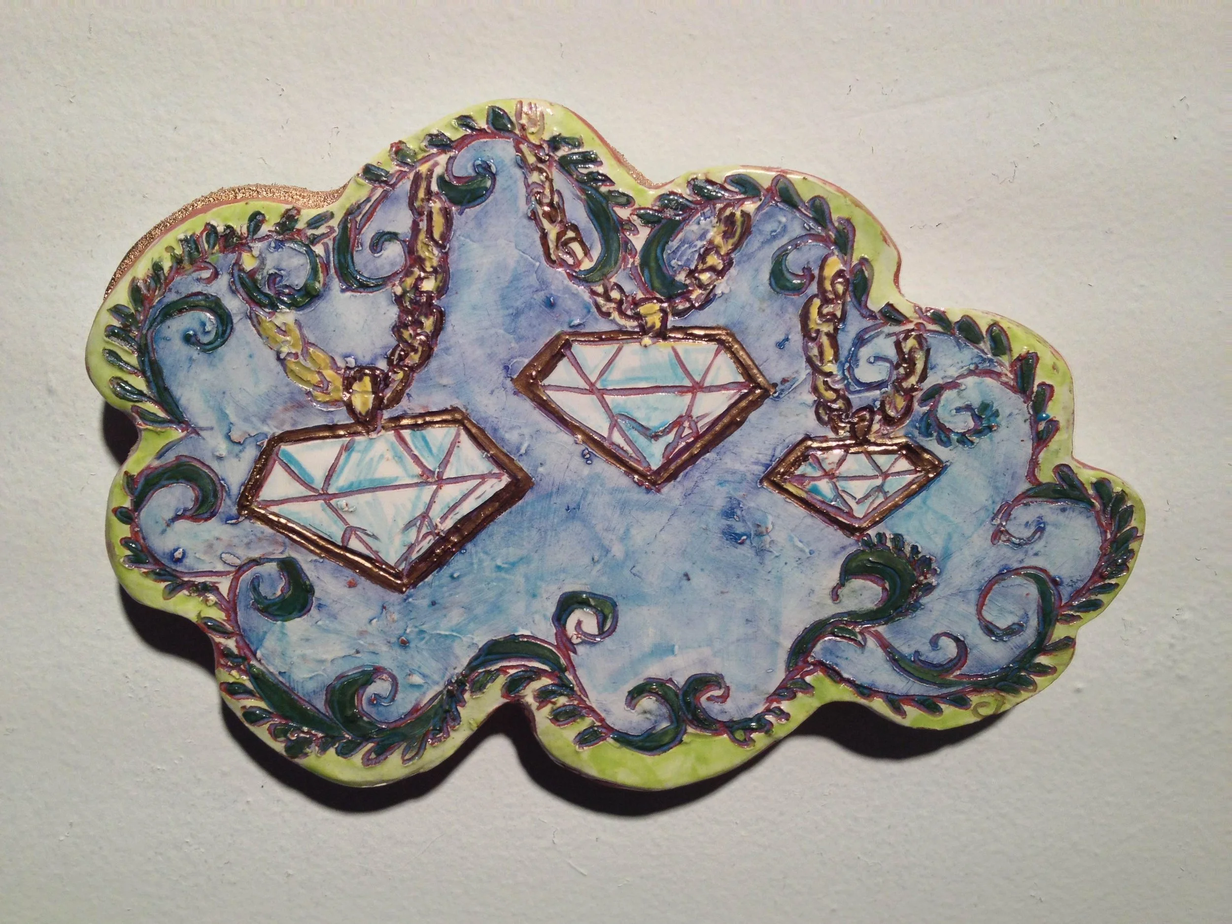 Decorative ceramic plate with blue background, ornate gold and black chains, and three diamond-shaped charms hanging from the chains.