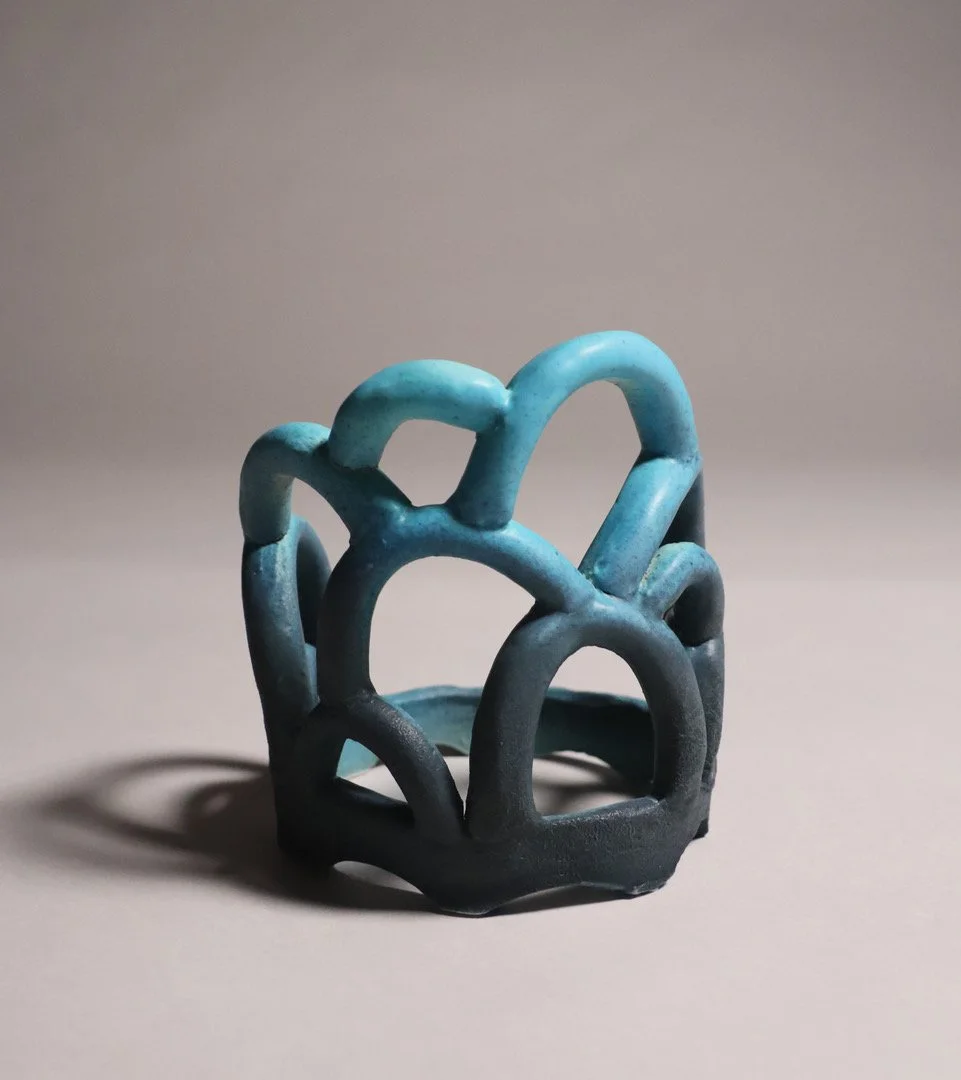 A modern, abstract blue and black ceramic sculpture with curved, looped shapes on a gray surface.