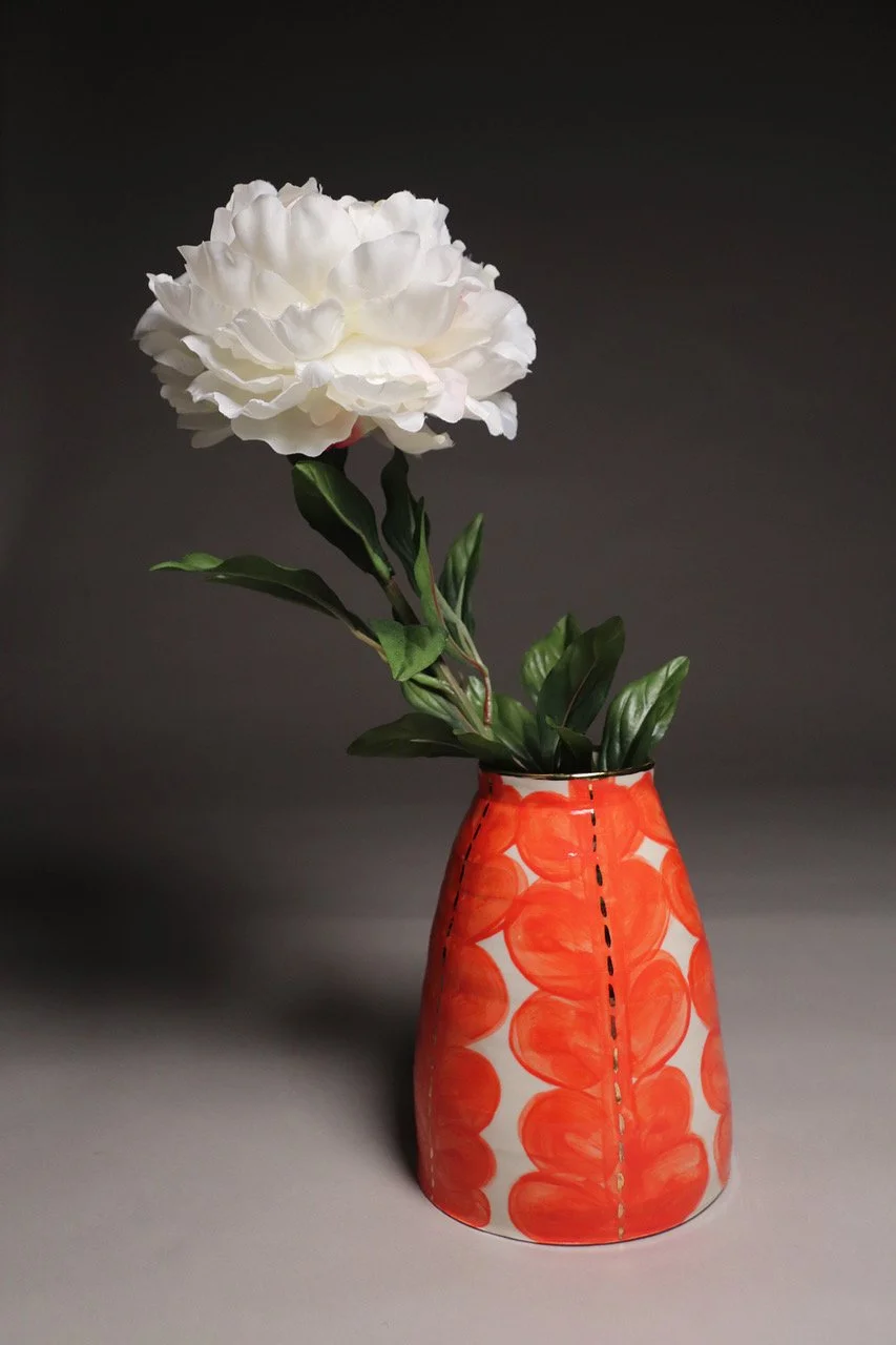 A white flower with ruffled petals in a colorful orange and white ceramic vase with orange circular patterns.