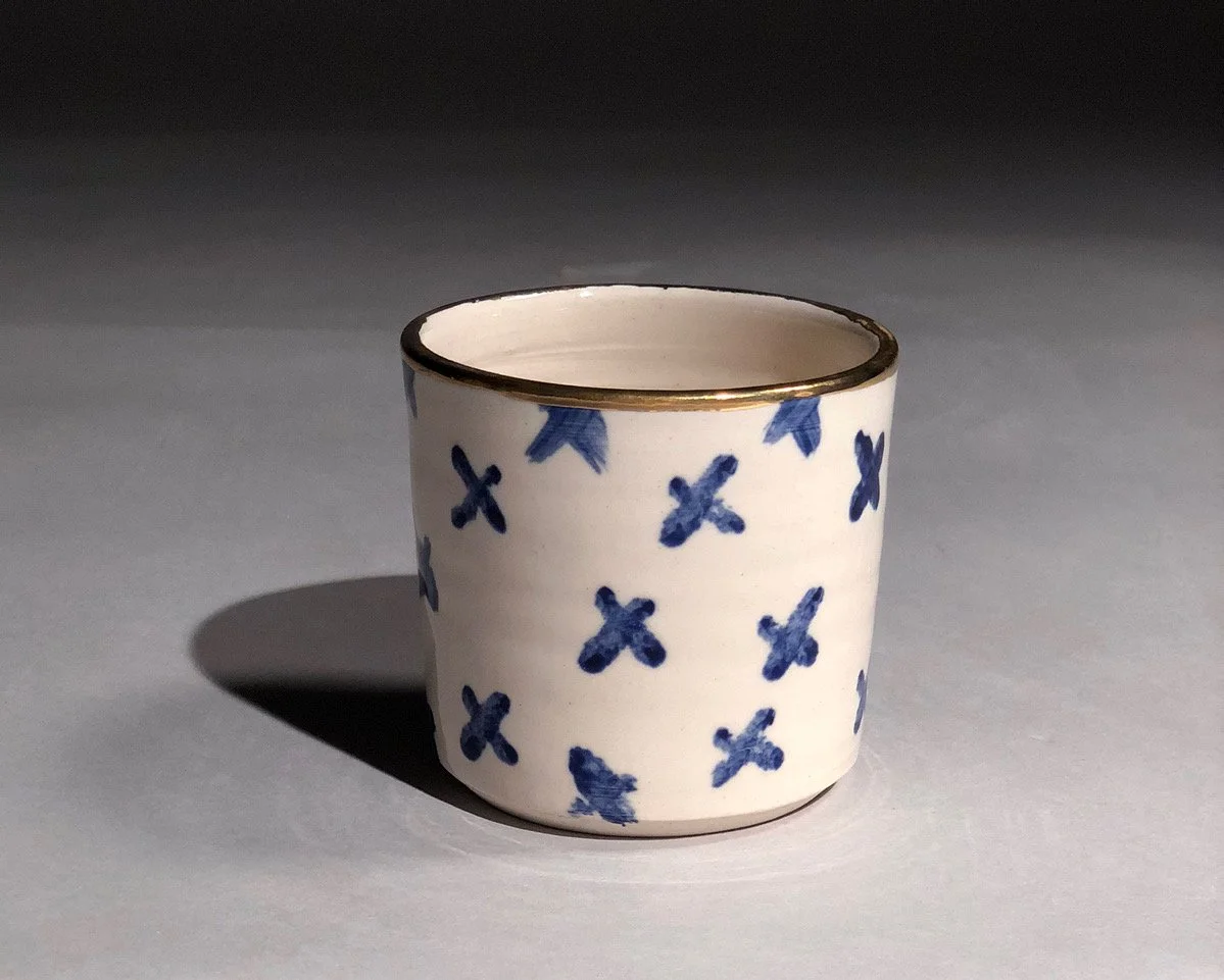 White ceramic cup with blue floral patterns and gold rim, casting a shadow on a gray surface.