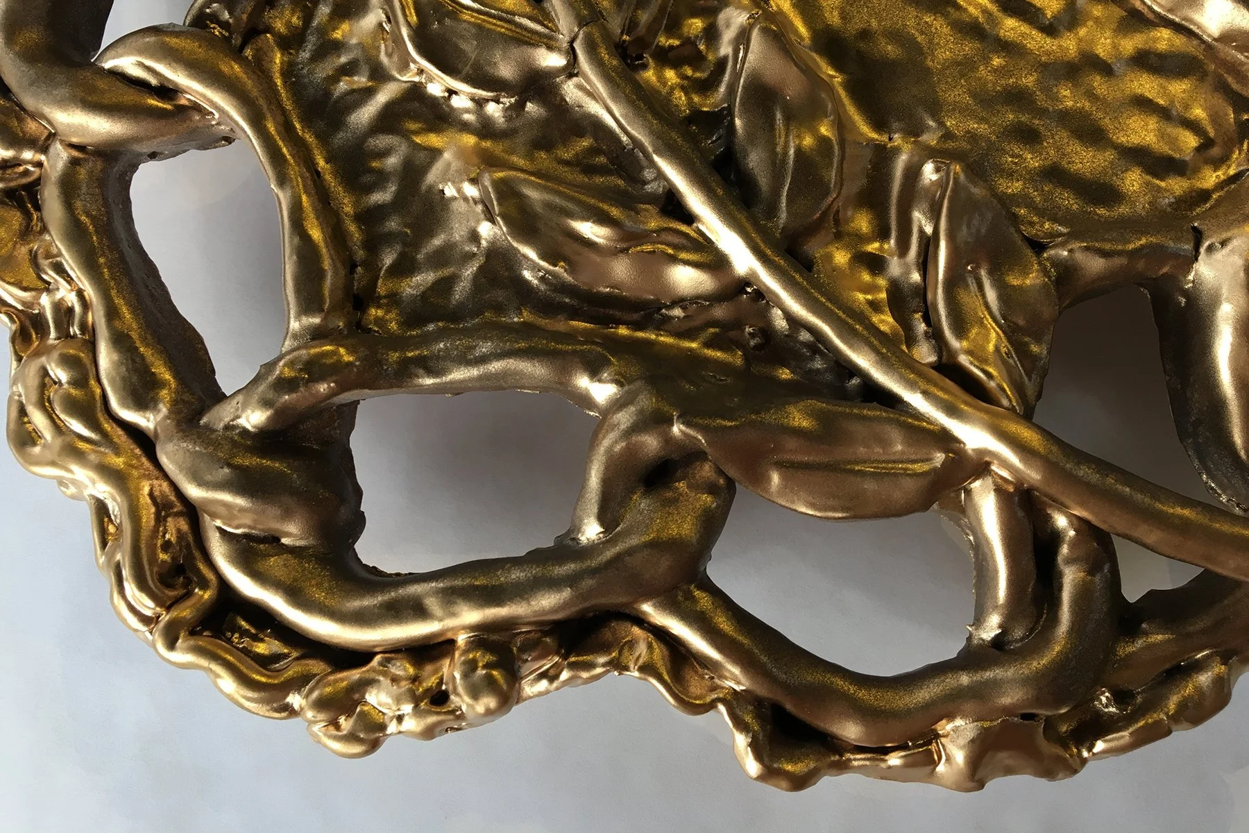Close-up of an abstract gold-colored metal sculpture with twisting, intertwined shapes.