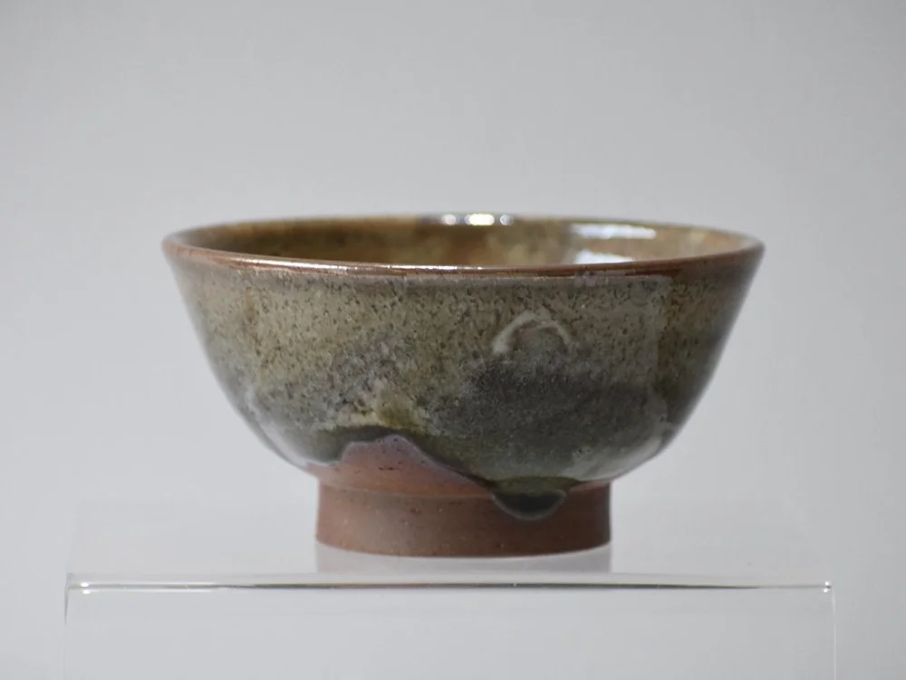 A ceramic bowl with a mottled earthy glaze on display in a museum setting.