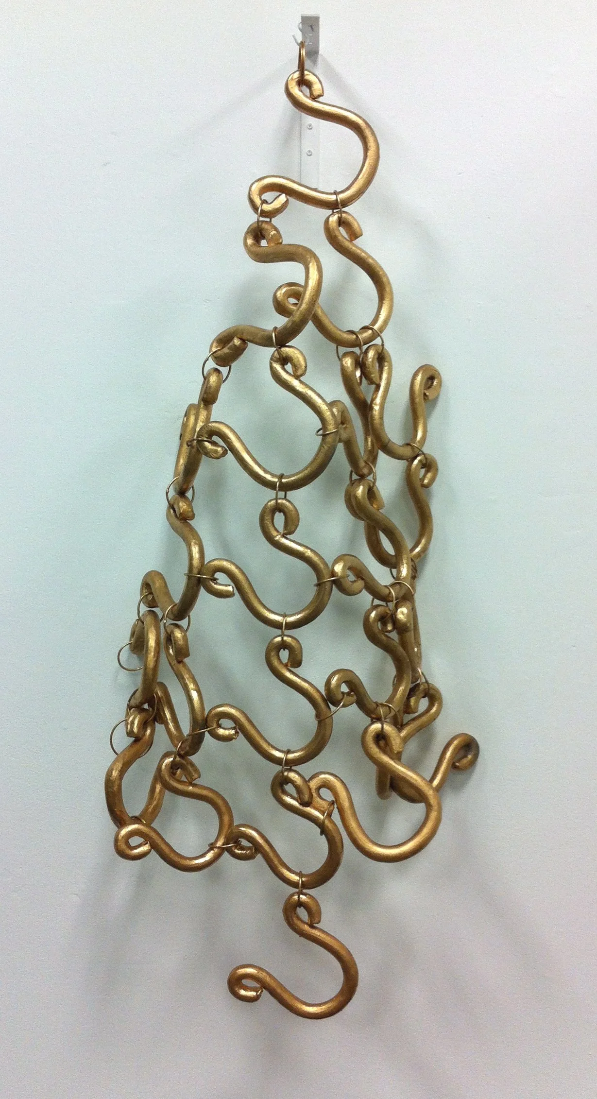 A decorative wall hanging made of interconnected gold-colored metal hooks arranged in a vertical, abstract pattern.
