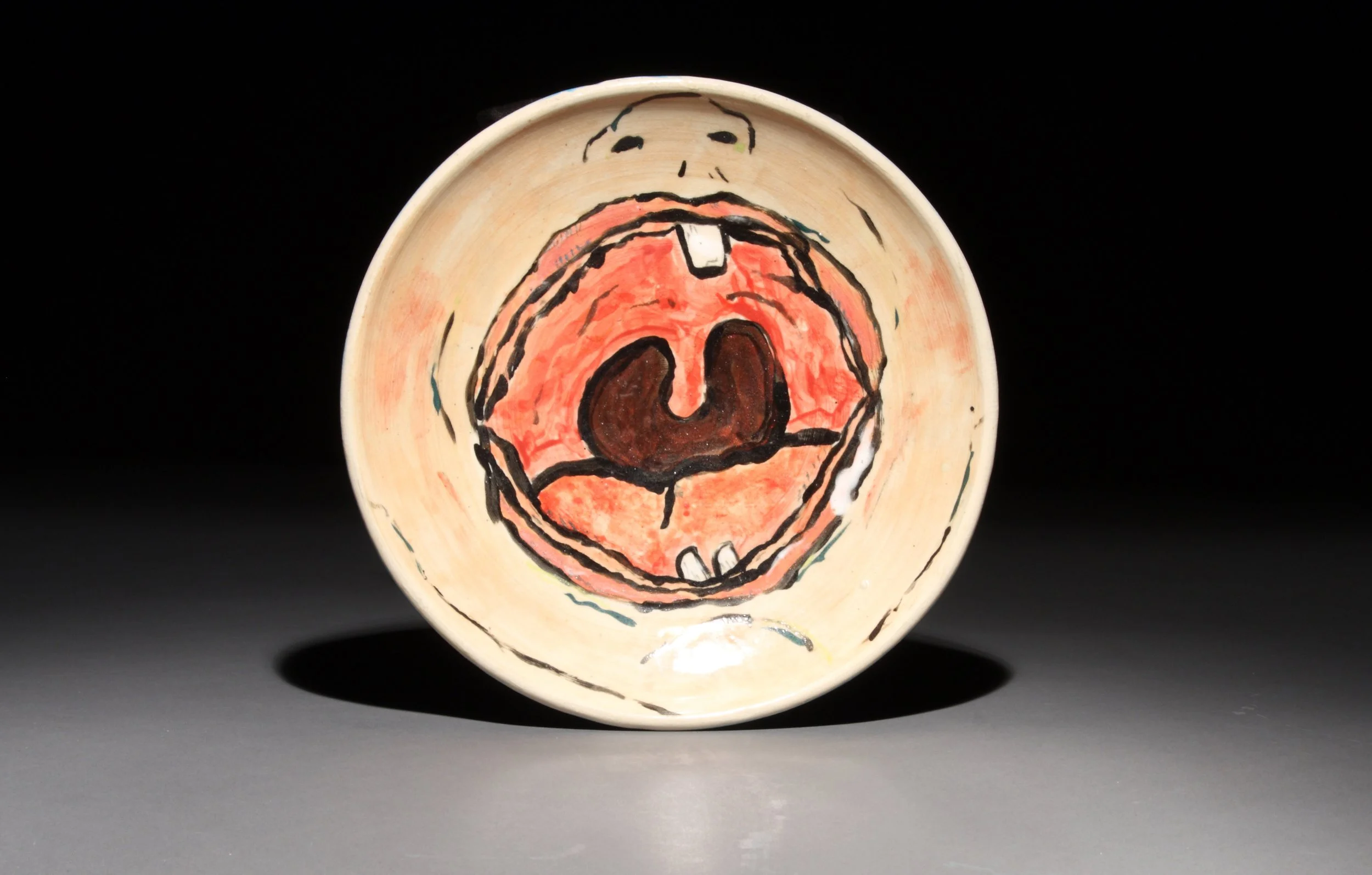 Ceramic bowl with abstract, expressive painting of a large open mouth with teeth and a nose, painted in bold black outlines, reds, and browns.