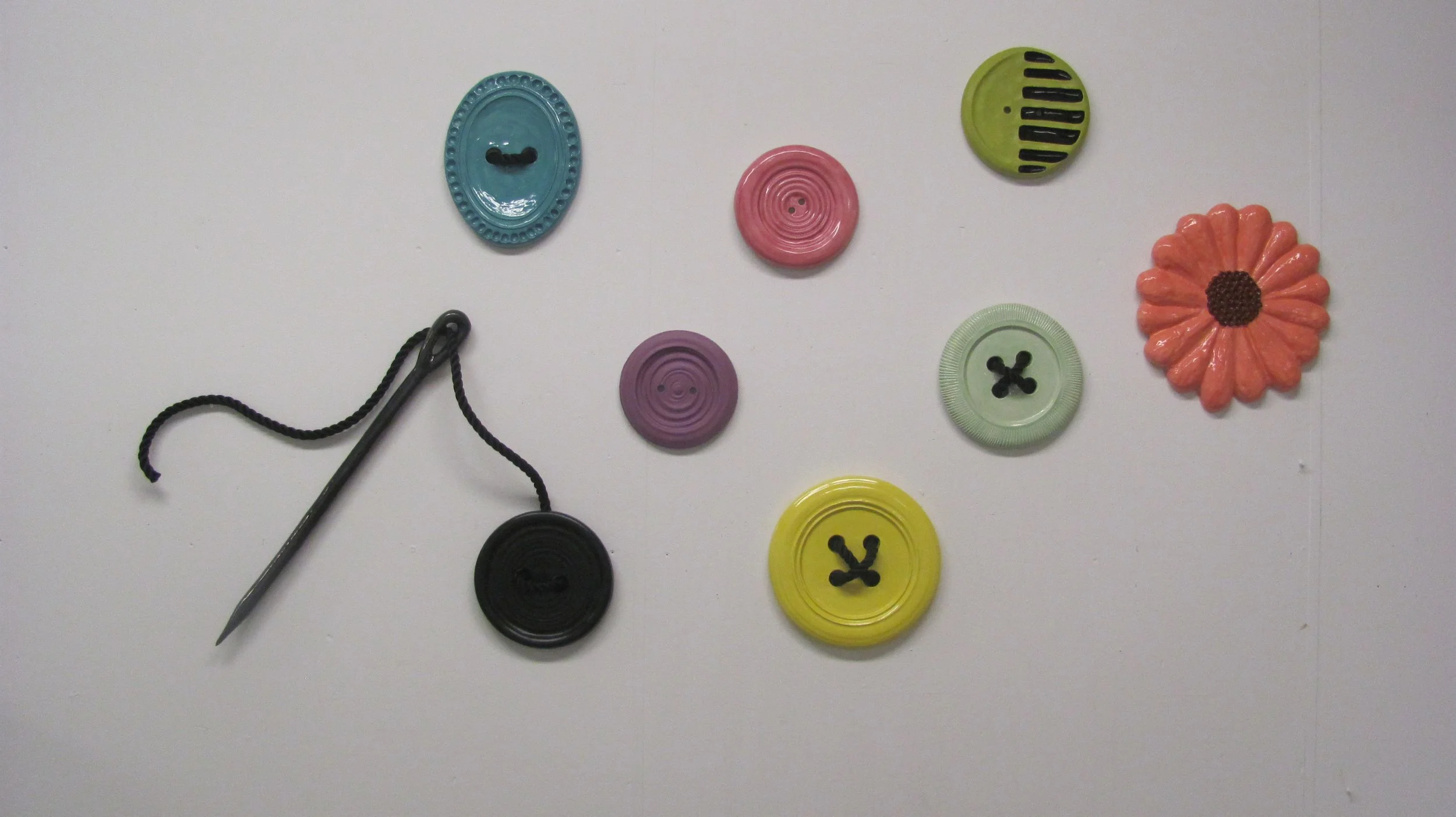 Colorful buttons arranged on a white surface along with a sewing pin with a black head and black thread.