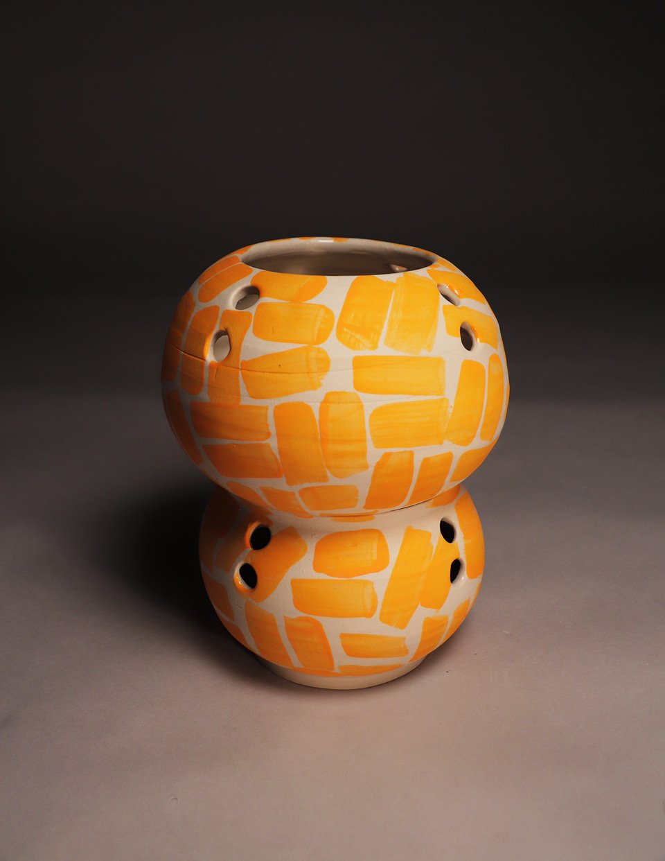 A ceramic double-decker oil diffuser with a white background and orange abstract shapes, sitting on a gray surface with a dark background.
