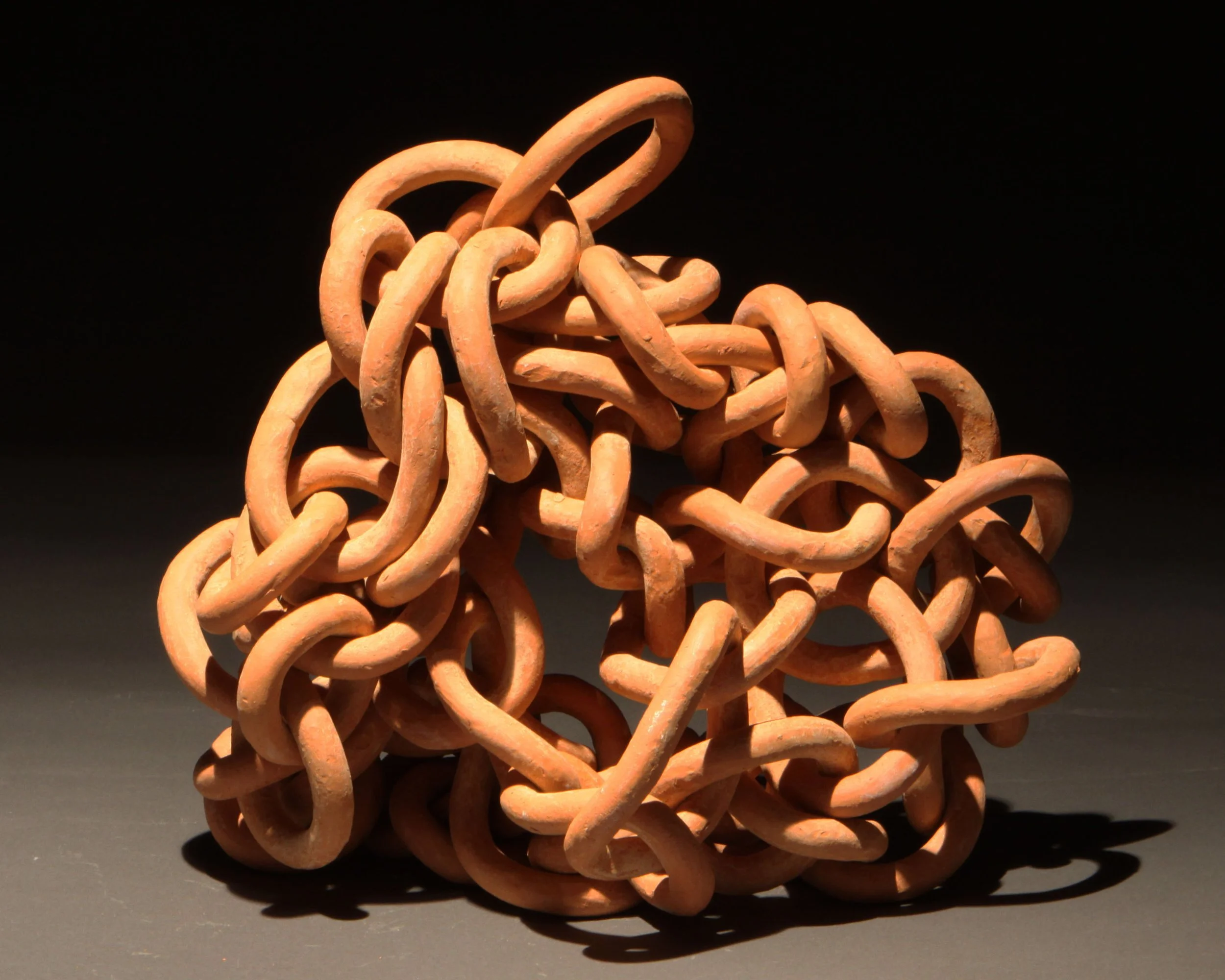A tangled pile of orange-brown clay or plastic links or chains on a dark background.