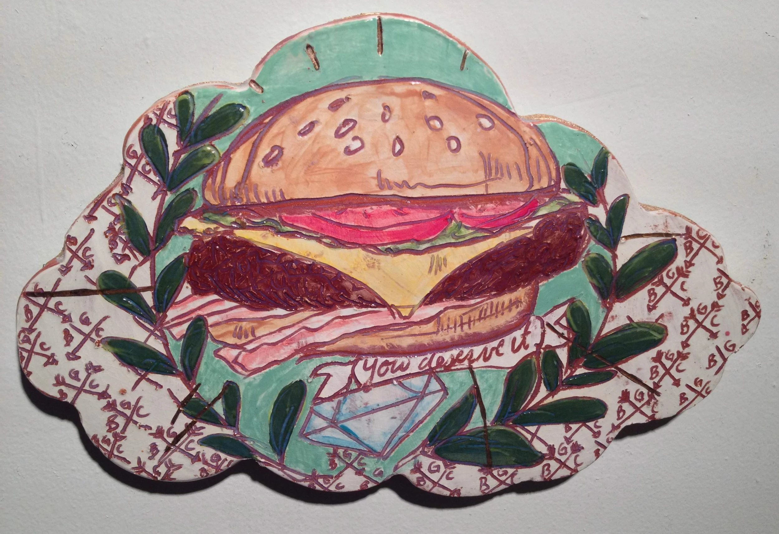 A colorful illustration of a cheeseburger with lettuce, tomato, cheese, bacon, and a sesame seed bun, surrounded by decorative greenery and a patterned background featuring a diamond and 'You deserve it' text.
