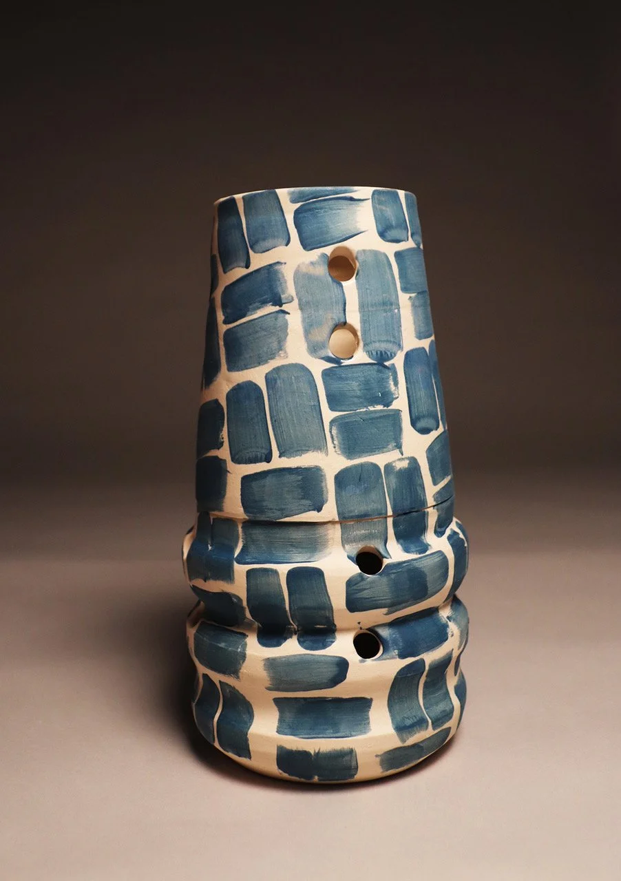 Ceramic sculpture with a white base and blue rectangular patterns, featuring multiple holes and an abstract, layered form.