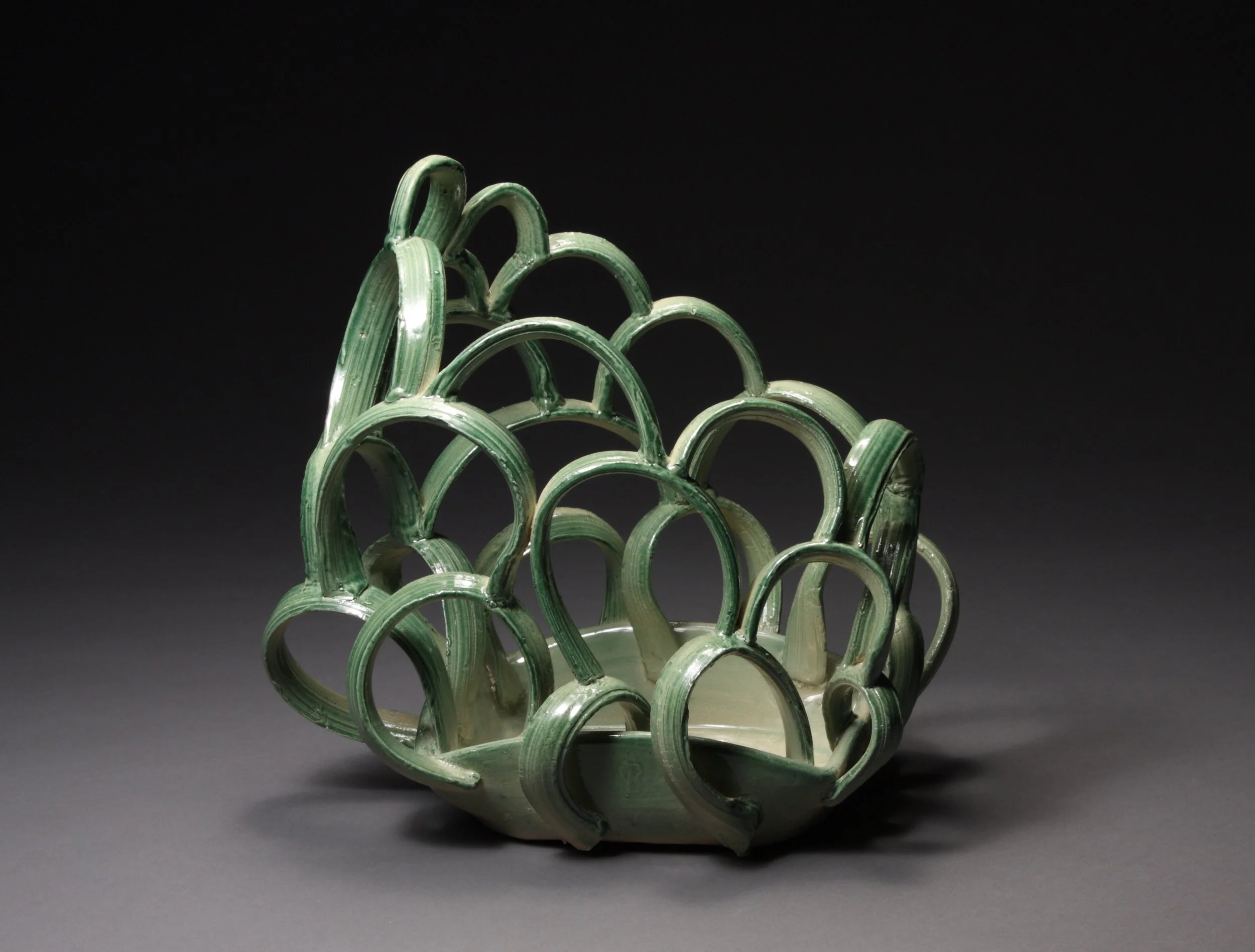 A decorative ceramic sculpture with an intricate open-work design of curved greenish striated loops.