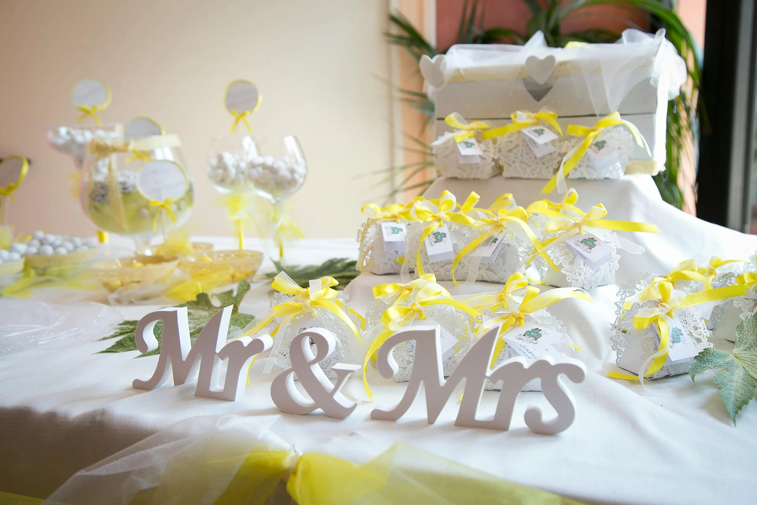 Decorated table with Mr. & Mrs. sign, yellow ribbons, white and yellow gift boxes, and candy jars at a wedding celebration.