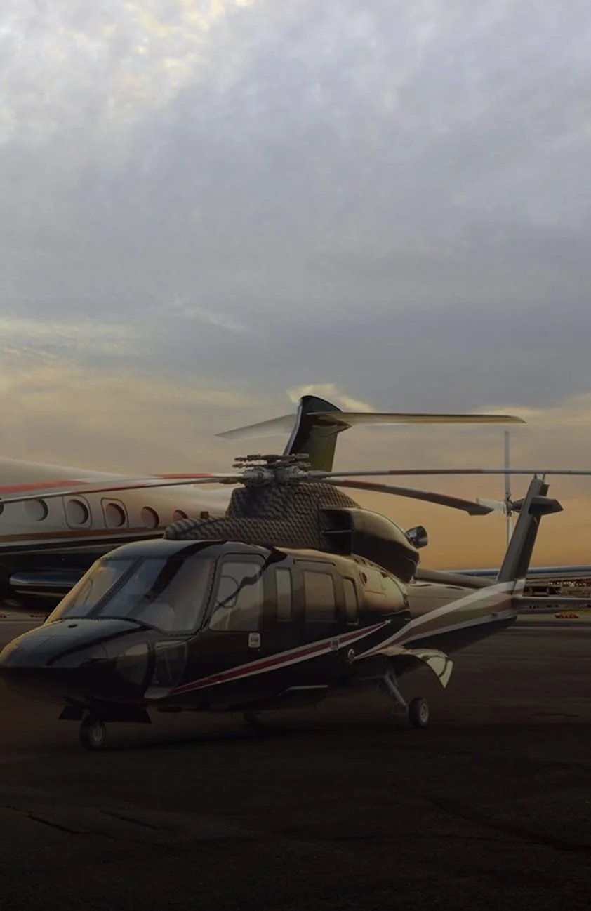 Black helicopter parked on an airport tarmac with a larger aircraft in the background, under a partly cloudy sky at sunset.