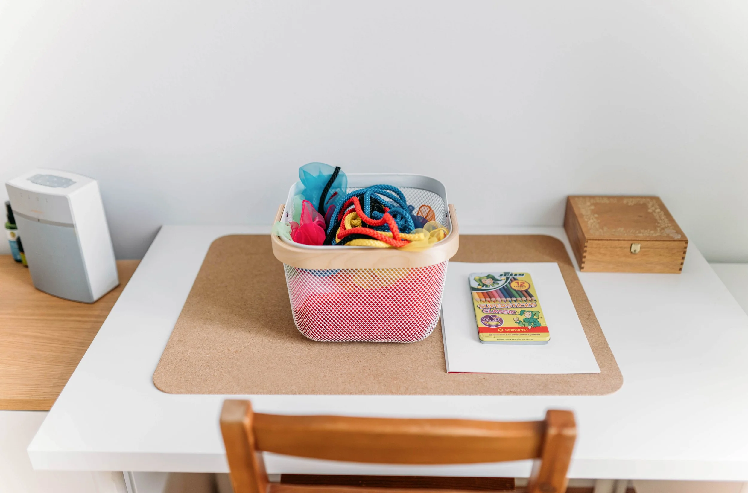 Ein Tisch mit Schulmaterialien, einschließlich eines Mülleimers mit bunten Schnürsenkeln, einem Notizbuch, einem Federmäppchen und einem Luftreiniger.