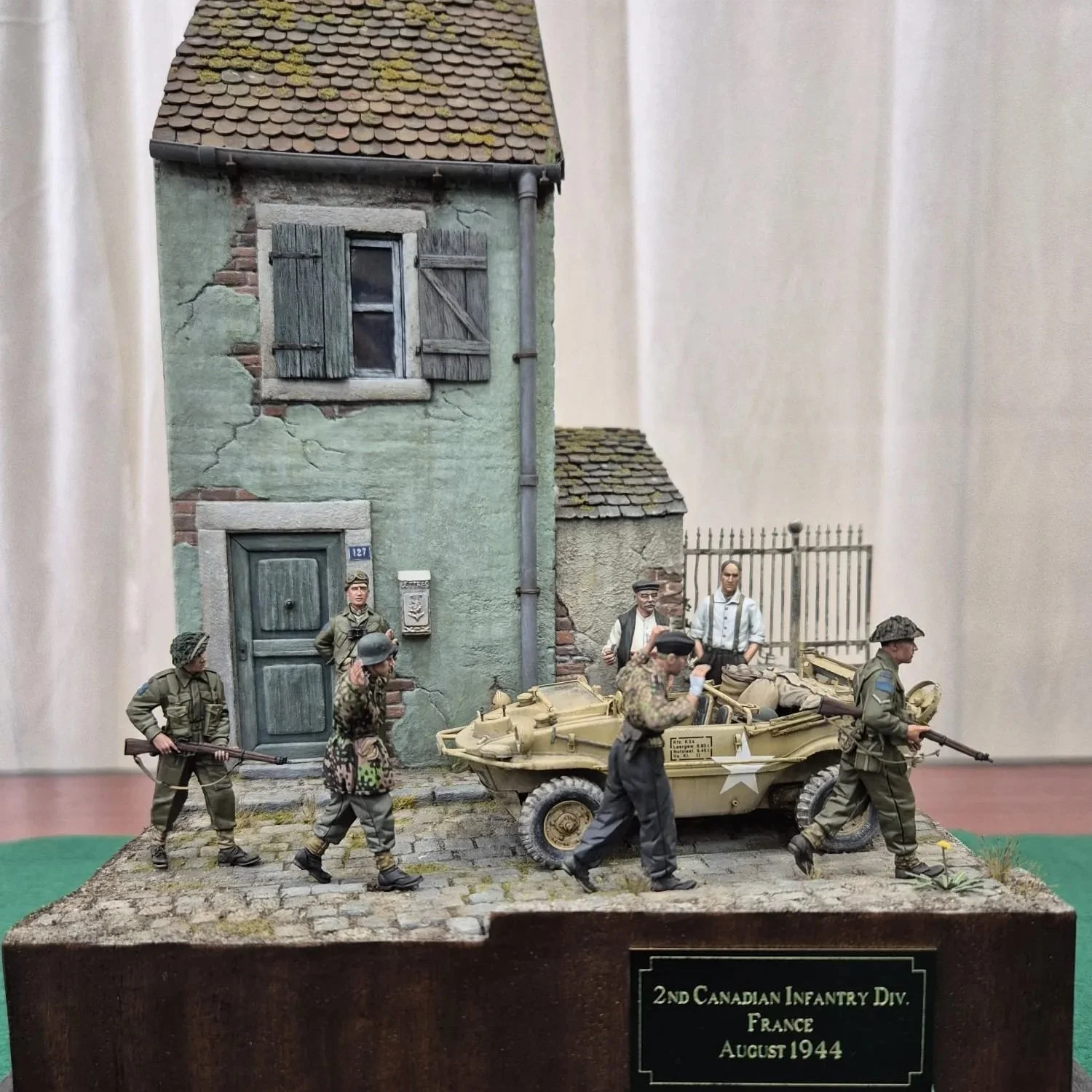 Miniature diorama of soldiers from the 2nd Canadian Infantry Division in France, August 1944, with a small building and a military vehicle on a cobblestone street.