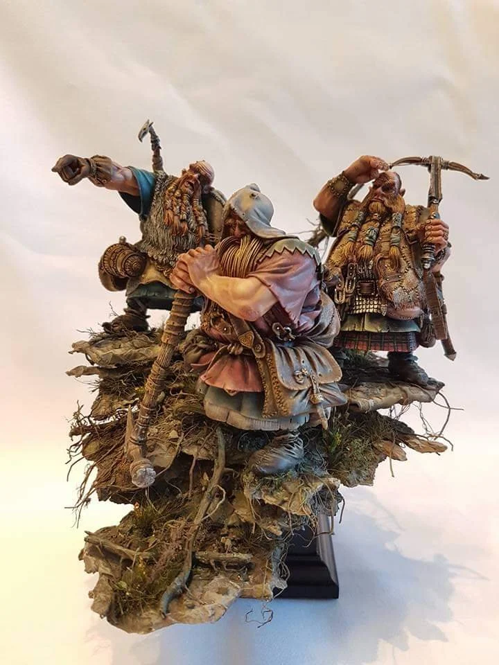 Detailed sculpture of three Viking warriors standing on a rocky base with grass and roots, holding weapons and dressed in traditional Viking attire.