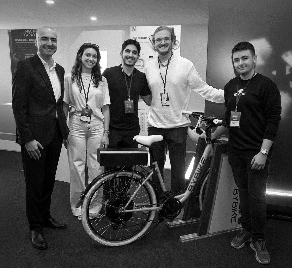 Group of five people standing around a bicycle and smiling at a technology event.