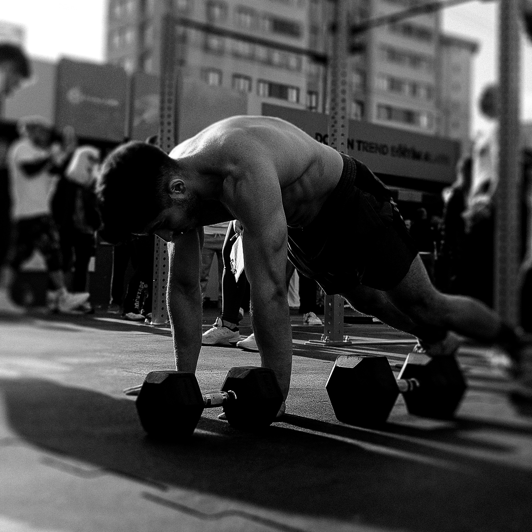 Man performing a plank with dumbbells on a city street during workout