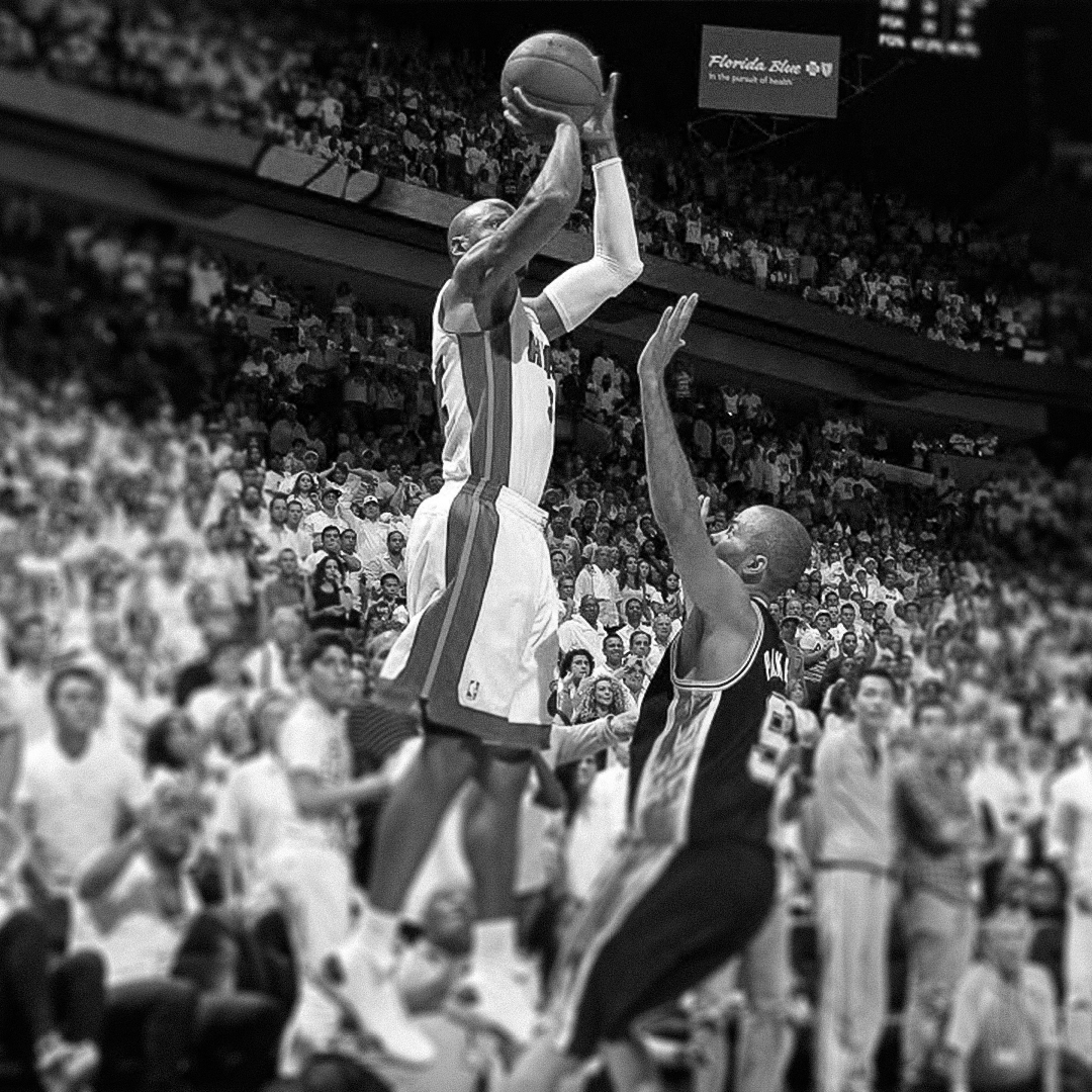 A basketball player from the Miami Heat jumping to shoot the ball, while a player from the Orlando Magic attempts to block the shot during a game in an arena crowded with spectators.