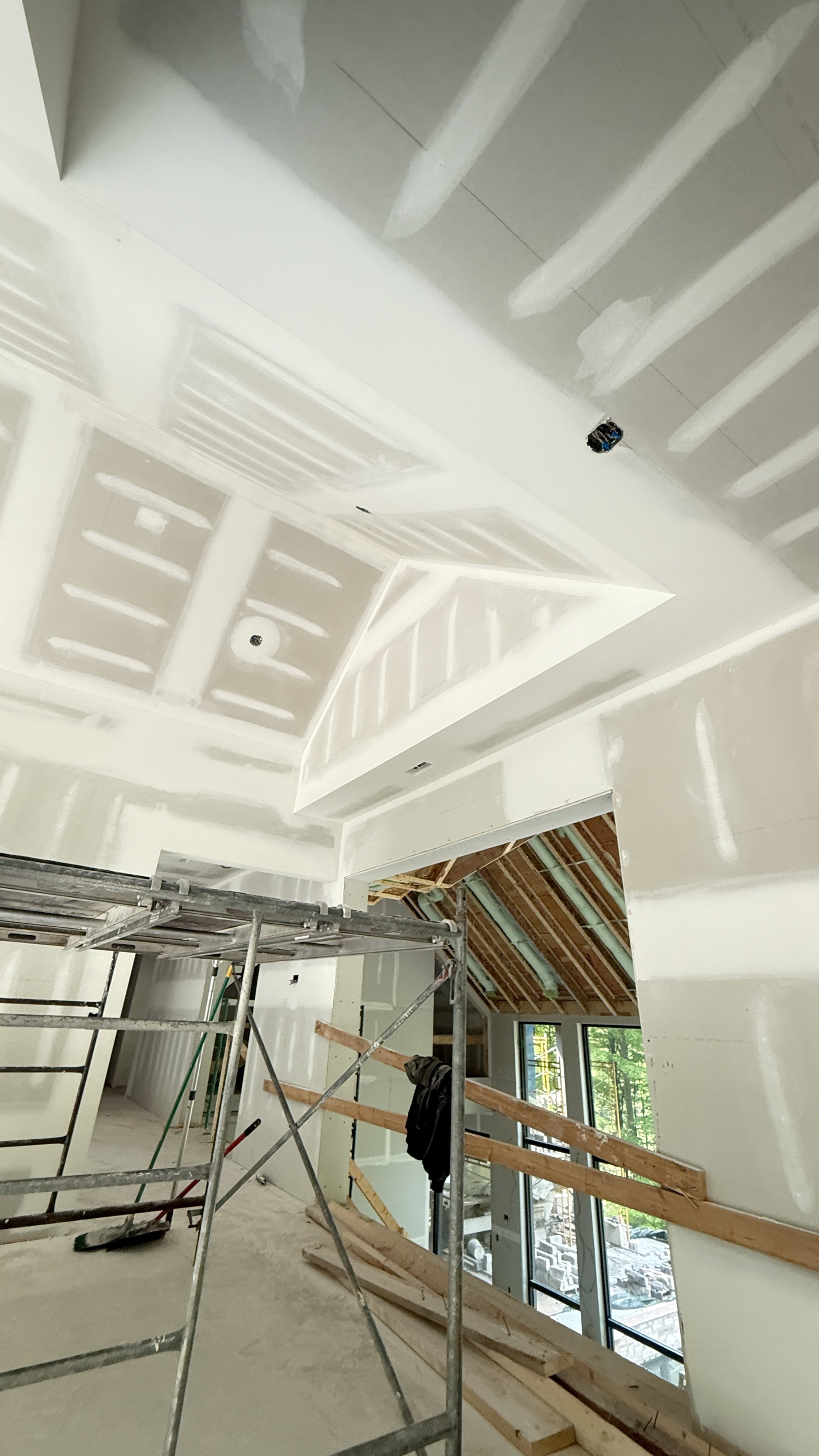 Interior view of a house under construction with unfinished drywall, scaffolding, and exposed roof framing.