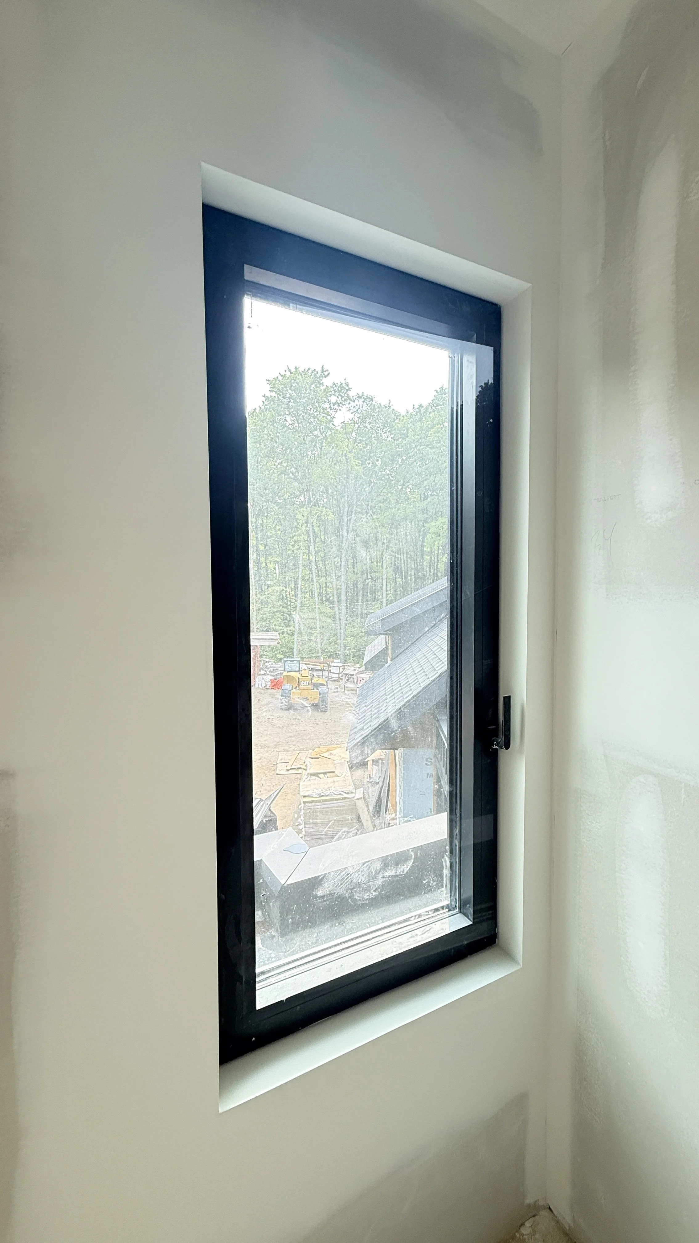 Close-up view of a black-framed, rectangular window installed in a white wall with a construction site visible outside.