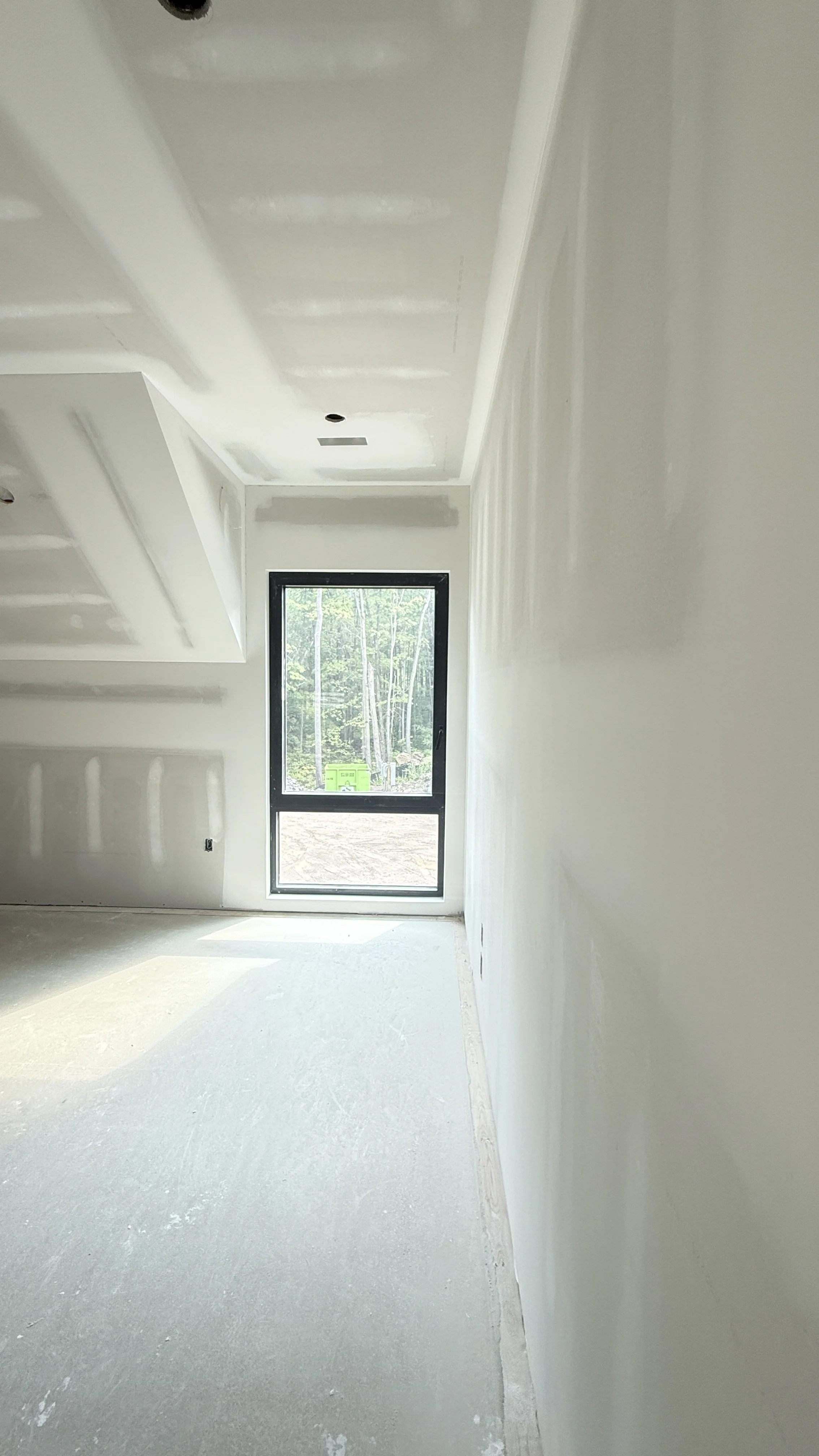 An unfinished room under construction with drywall installed, a window showing trees outside, and a bare floor.